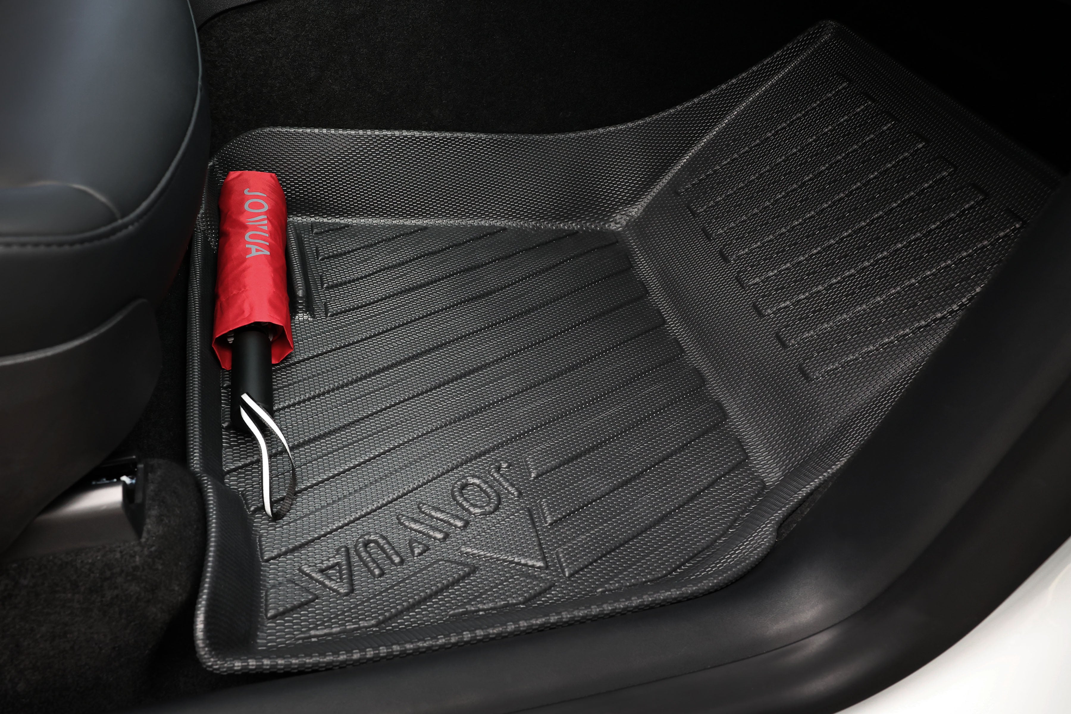 汽車內部有方向盤、黑色和木質儀表板以及帶有杯架和隔間的中央控制台。底部可見橡膠地墊。.