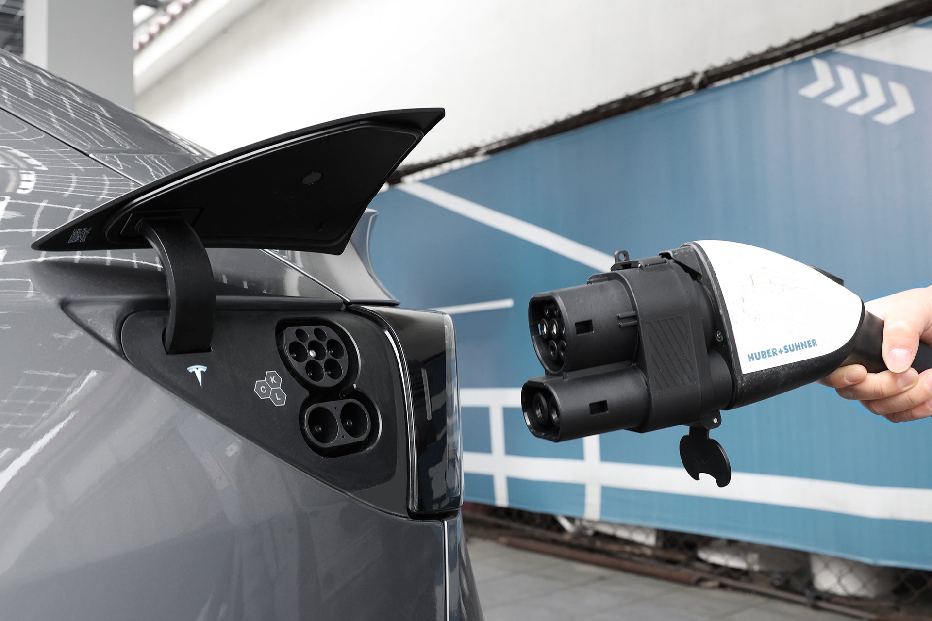 正在充電的白色電動車的特寫。充電器插入車輛的充電端口,有可見的綠色指示燈。背景是模糊的灰色表面。.