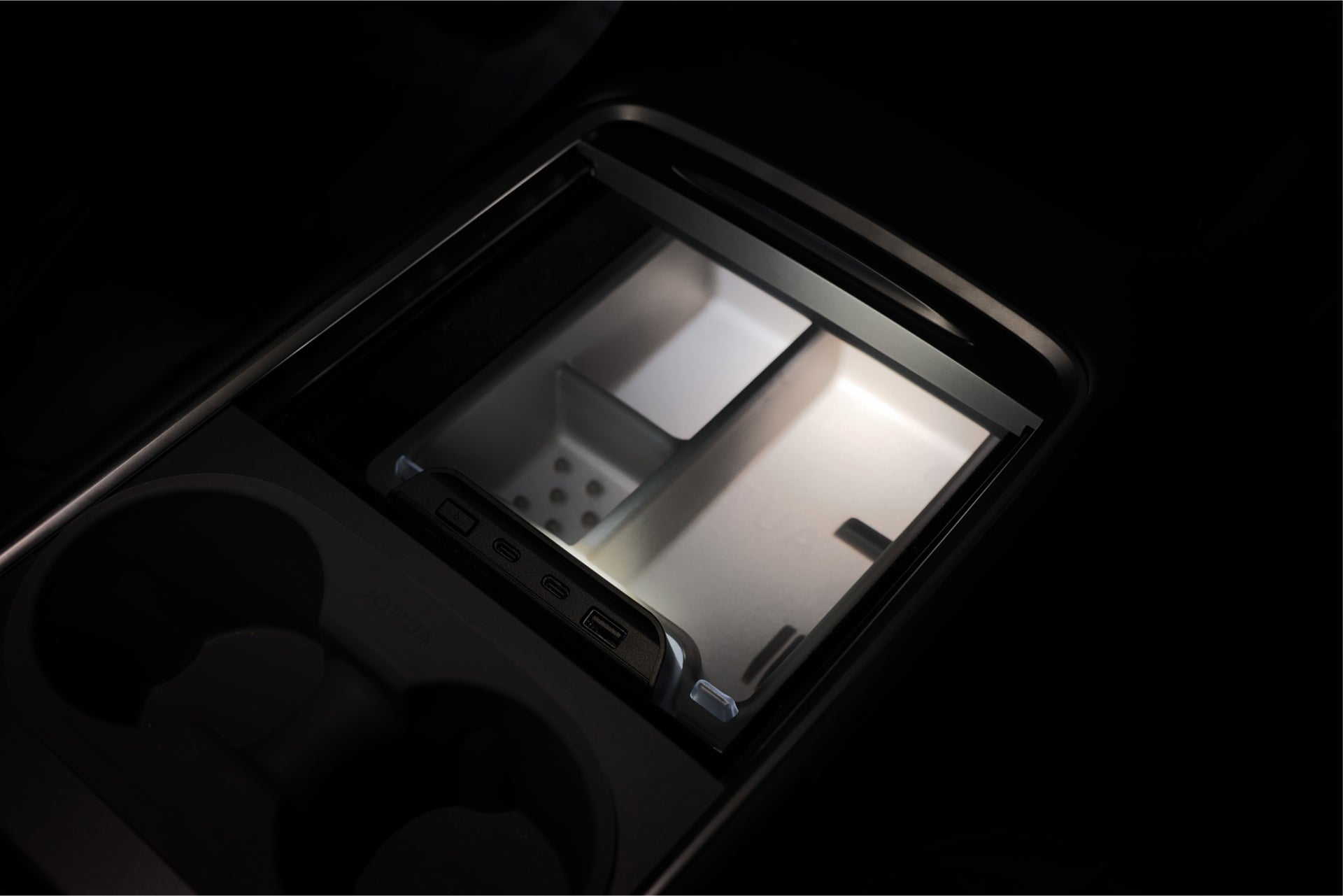 JOWUA 台灣 LED 中控組合的照明中控台特寫,配有帶 USB 連接埠和無線充電板的中控台收納室,在前景中露出杯架,增強了便利性和功能性。.