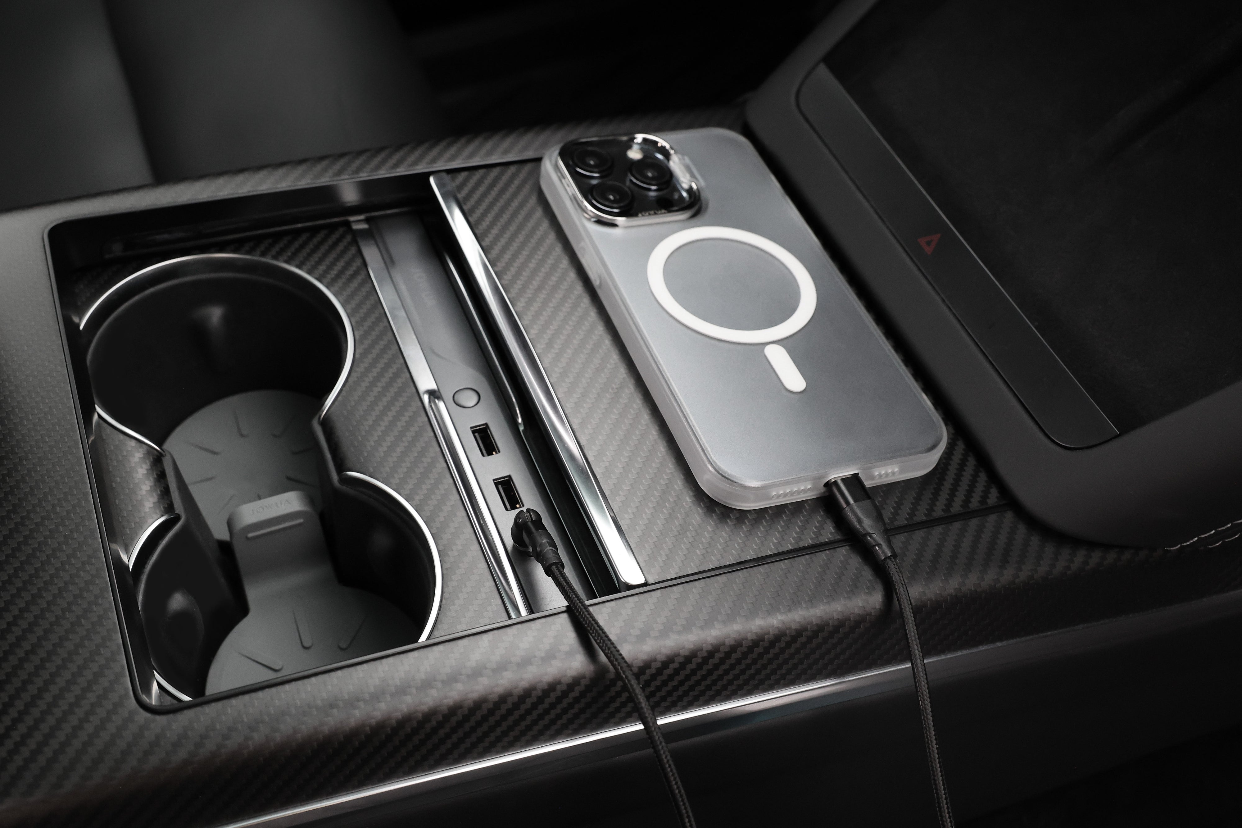 特寫 Model 3 中控台,採用碳纖維飾面,兩個杯架,USB 連接埠配備 JOWUA 台灣 USB-C 車用磁吸線,可進行 PD 快充充電,以及透過無線充電板上的電纜連接的智慧型手機。.