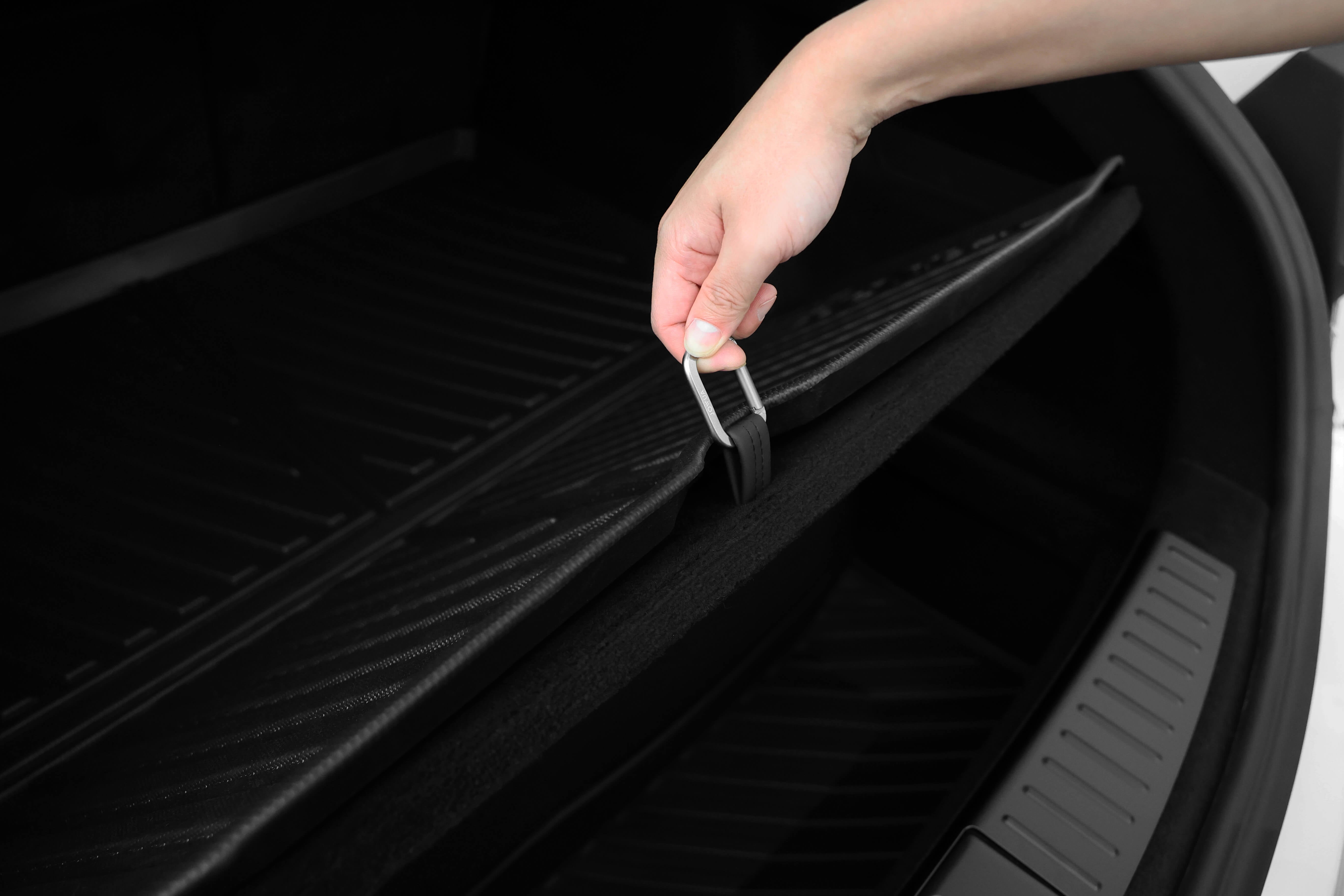 一隻手抬起了JOWUA台灣立體防水行李廂墊(Model S)適用於2023+特斯拉Model S的後備箱,展示了其帶有紋理的黑色表面。加厚材質設計提高了耐用性,因為光線可以從寬敞的內部空間反射出來。.
