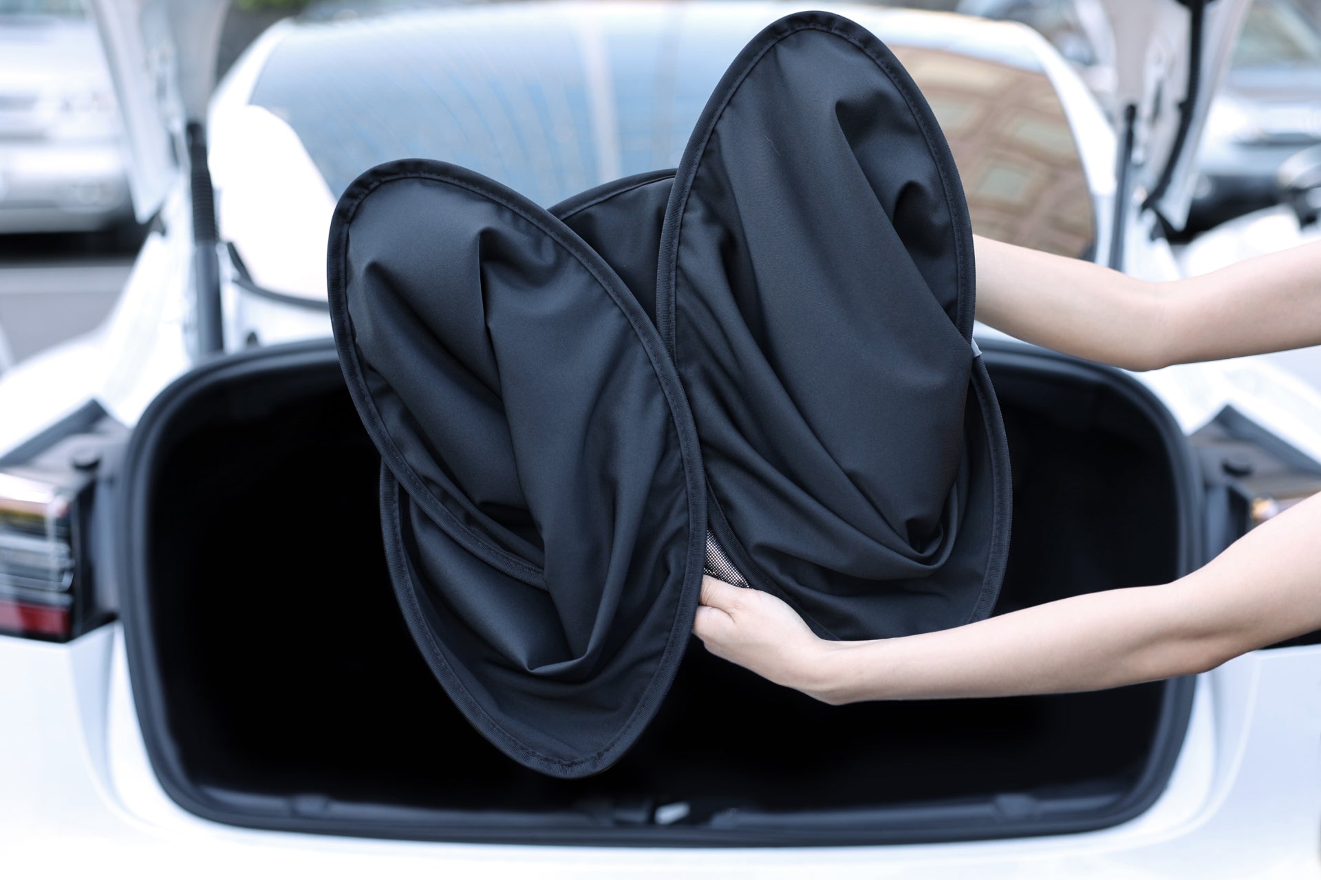 在城市背景的襯托下,兩手握住 JOWUA Taiwan 出品的扭曲形玻璃車頂遮陽簾 (Model S)。這款時尚的配件以其抗紫外線功能而聞名,在提供出色的防曬保護的同時,也增添了一絲黑武士風格。.