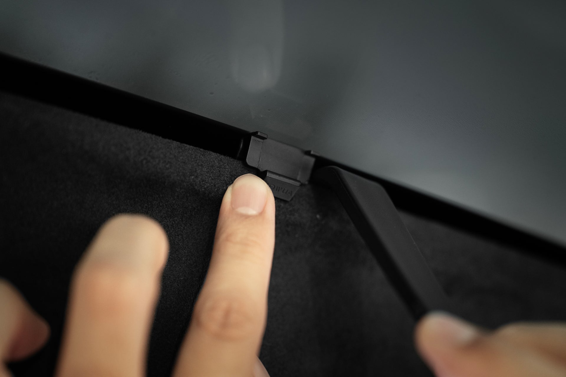 一隻手正在按下 JOWUA 台灣 Model X 分離式遮光簾組件邊緣的一個小黑色按鈕,該按鈕位於螢幕和霧面黑色邊框之間。.