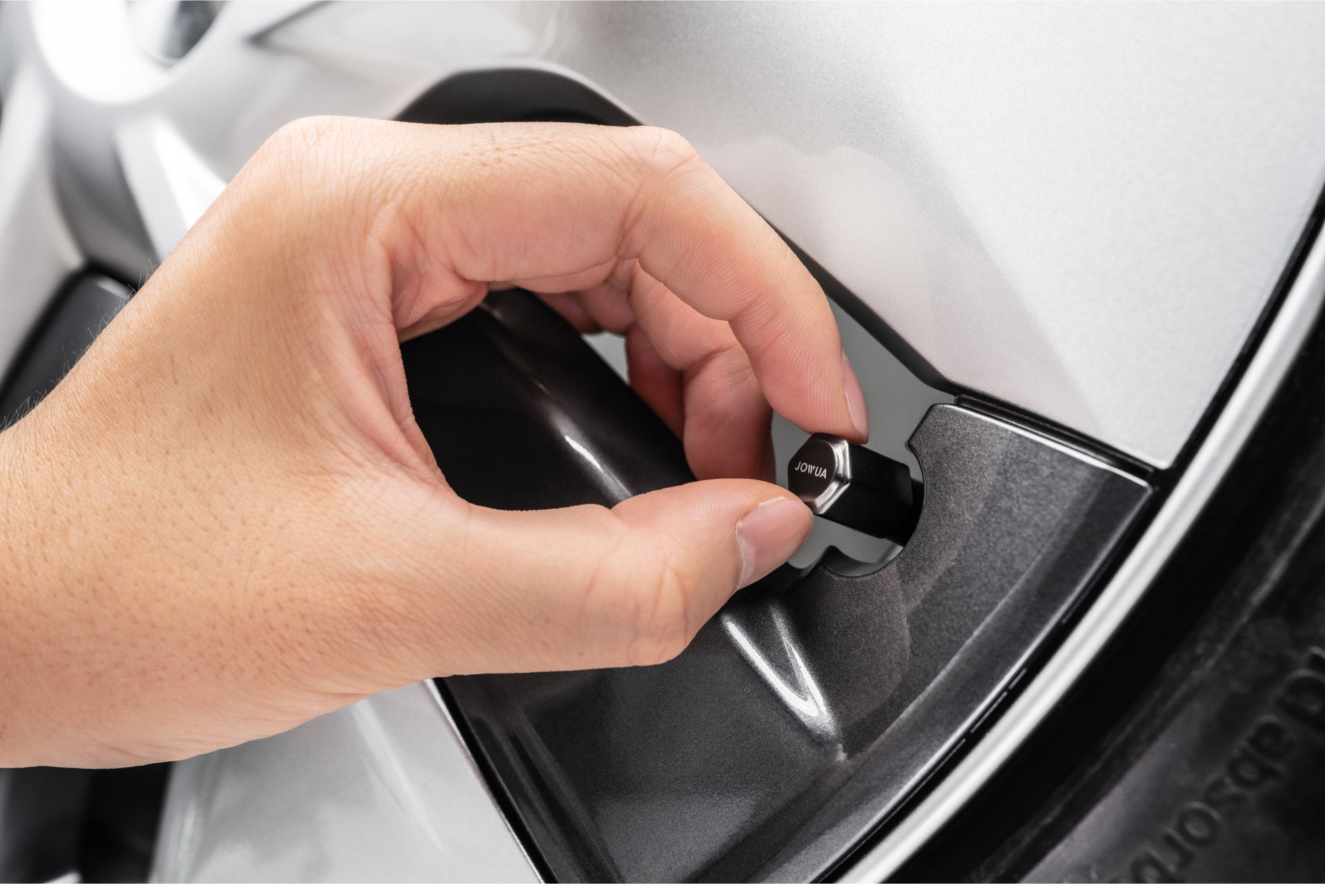 一隻手轉動銀色汽車油箱蓋上的旋鈕,外部和輪胎清晰可見——體現了JOWUA台灣打氣機充電組合為需要在旅途中快速、可靠充電和充氣的用戶提供的便利性。.