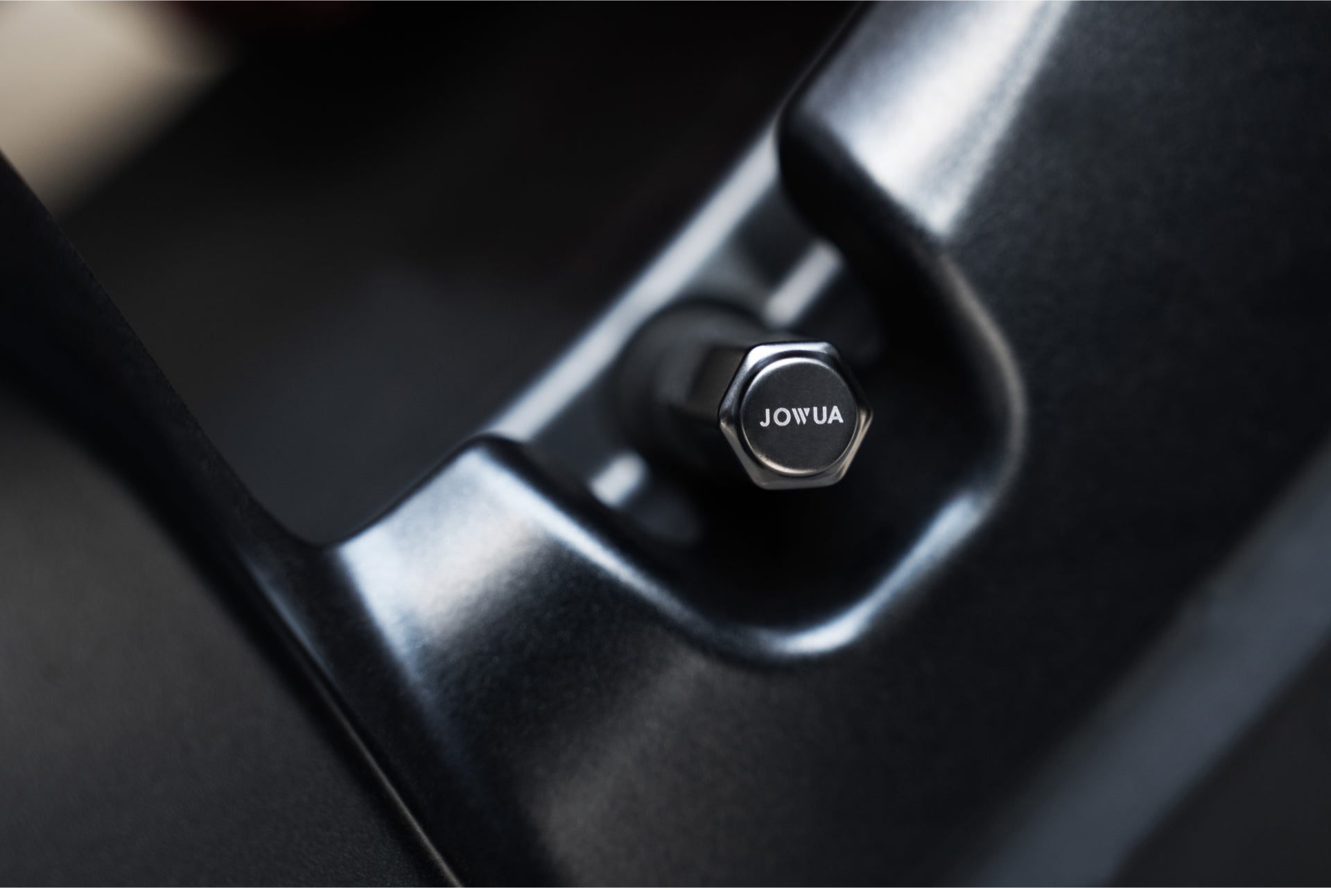 頂部刻有 JOWUA 台灣字樣的金屬旋鈕特寫,安裝在黑暗的固定裝置中 — 可能是打氣機充電組合的一部分。.