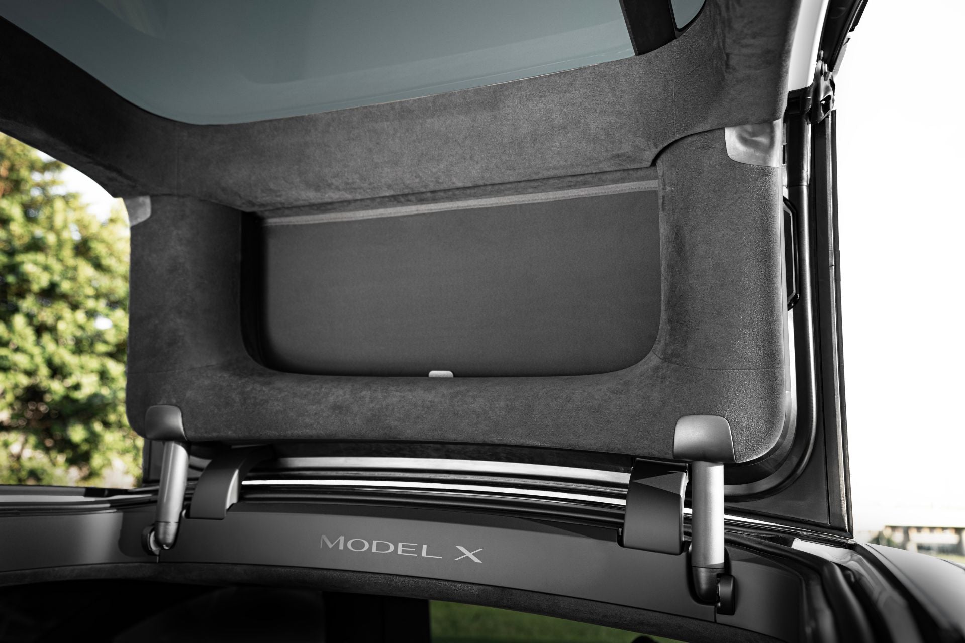 特斯拉 Model X 後掀門打開的特寫,顯示已安裝 JOWUA Taiwan 分離式遮陽簾。後備箱、內襯及全景玻璃車頂清晰可見,背景為樹木與天空。.