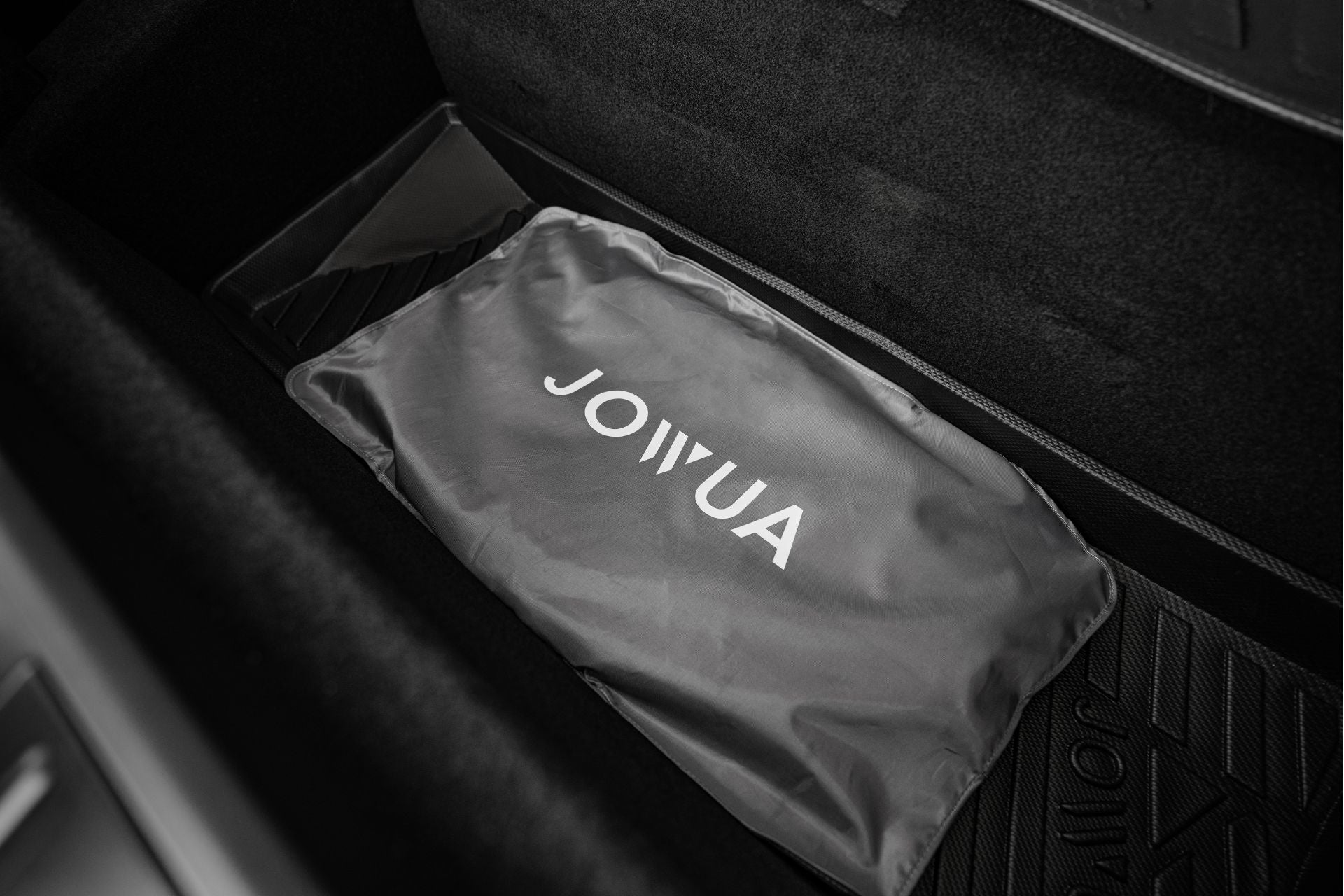 黑色 Model X 後備箱特寫,其中標有“JOWUA”的灰色袋子放置在橡膠墊上,採用 JOWUA 台灣分離式遮陽簾,提供卓越的隔熱效果,讓您的物品在乾淨整潔的內部保持涼爽舒適。.