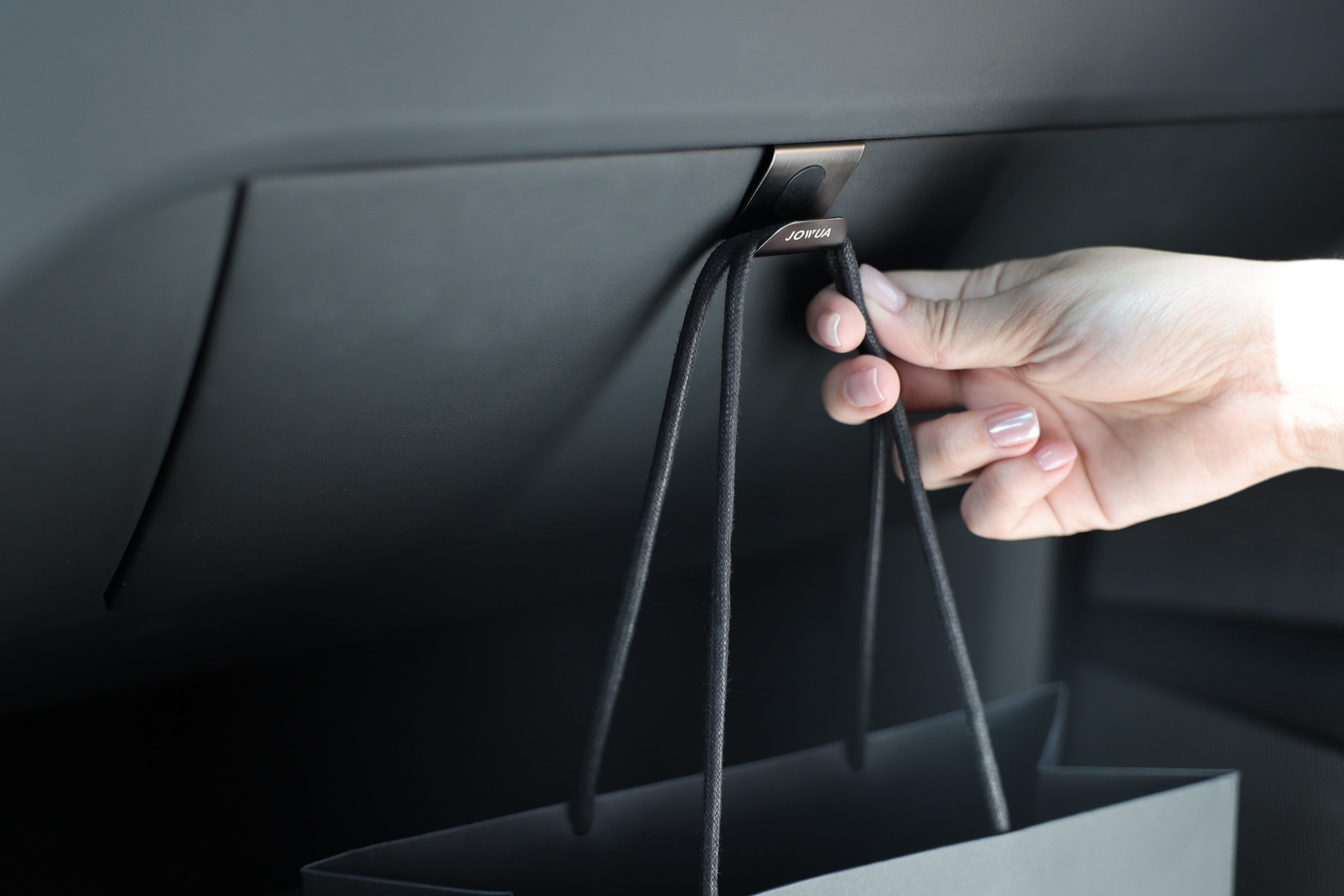 一隻手在 Model 3 內的手套箱掛鉤上掛著一個黑色購物袋,展示了 JOWUA 台灣的創新收納解決方案。.