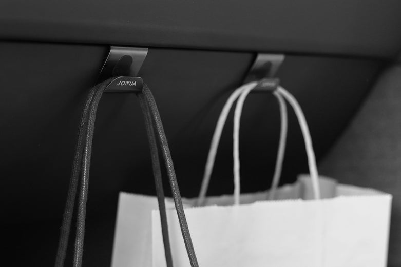 兩個購物袋掛在黑暗表面下的金屬掛鉤上,可能是在車內。黑白圖片強調 JOWUA Taiwan 的一幕瞭然【Model 3/Y 煥新版|交車禮包】,特斯拉的配件,方便收納。.