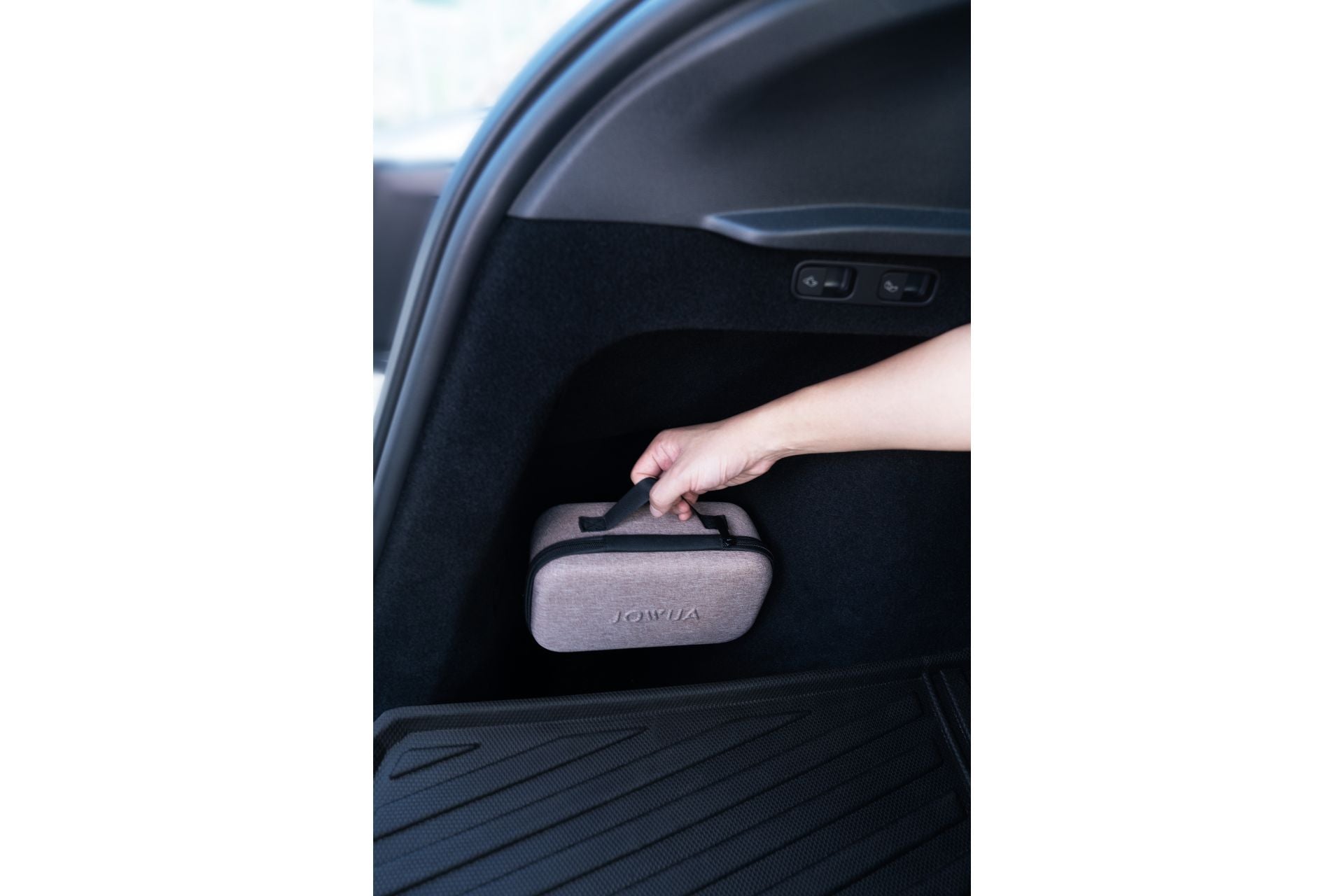 一隻手將一個灰色的 JOWUA Taiwan 箱子從後車廂的儲物格中取出或放置--非常適合存放 Tesla 配件,如 100W 雙快充打氣機,包含在安心組合【Model Y 煥新版|交車禮包】中。.