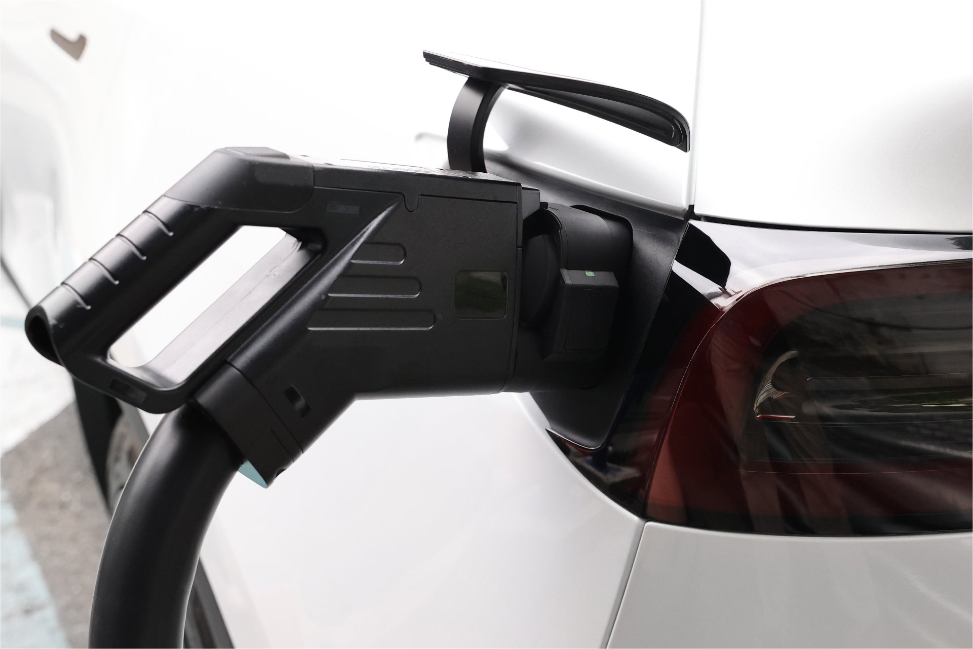 白色汽車使用 JOWUA Taiwan CCS2 快慢充萬用組(通用版)進行交流充電的特寫,使用 J1772 轉 CCS2 轉接器和充電線插入後方連接埠。.