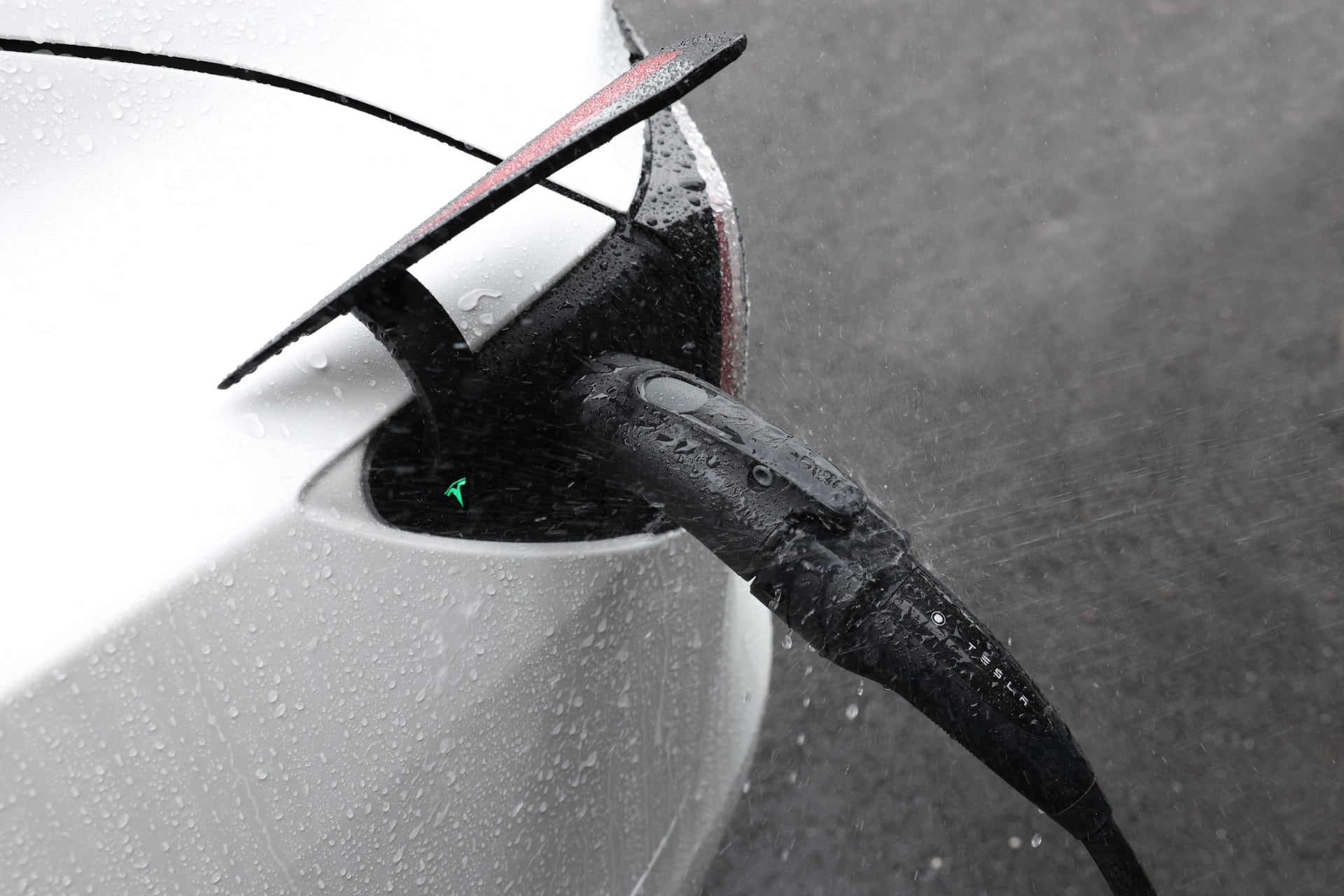 特寫:JOWUA 台灣 CCS2-AC (TYPE 2) 至 TPC(NACS) 轉接頭正在使用中,在雨中為電動車充電。電纜和車輛上的水滴凸顯了潮濕的環境。.