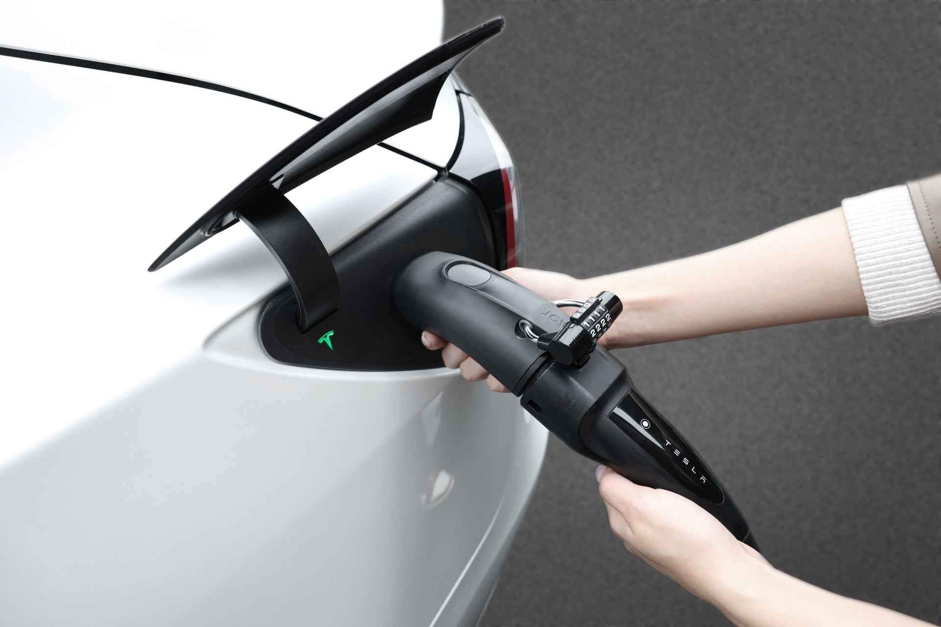 一個人將 JOWUA 台灣 CCS2-AC (TYPE 2) 至 TPC(NACS) 轉接頭適配器連接到電動車。影像突出顯示了拿著充電插頭的手和汽車充電埠上的綠燈,表示充電狀態良好。光滑的白色轎車在灰色背景的映襯下。.