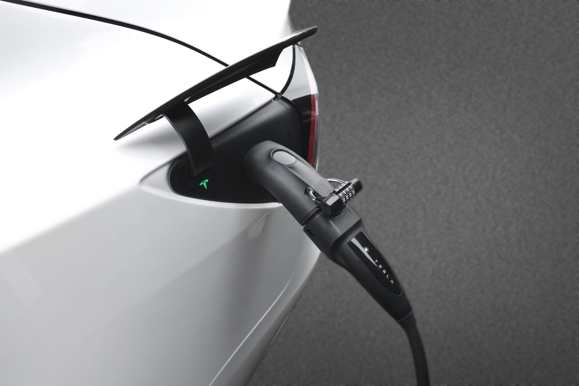 圖中 JOWUA 台灣 CCS2-AC(TYPE 2)至 TPC(NACS)轉接器連接一輛白色電動車,綠燈亮表示充電成功。該車的流線型設計在純灰色背景下顯得格外突出。.