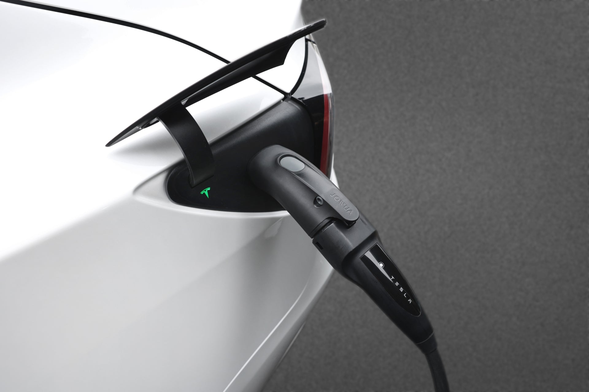 白色電動車,可能與JOWUA台灣CCS2-AC(TYPE 2)至TPC(NACS)轉接頭相容,使用黑色電纜充電。端口附近發出綠光,符合 IEC62196-2 標準。其光滑的空氣動力學設計引人注目。.