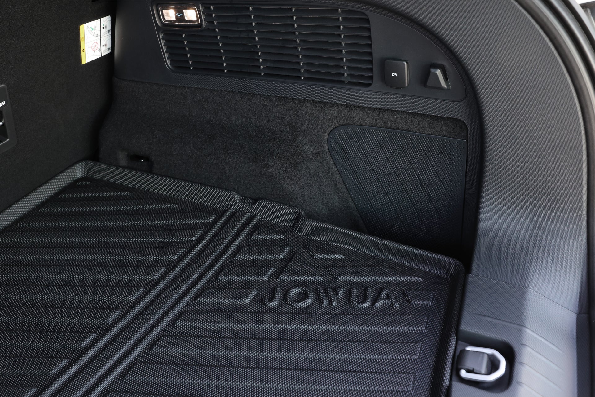 福特野馬 Mach-E 後備箱內部特寫,帶有壓印有“JOWUA Taiwan”字樣的紋理橡膠墊。該區域包括揚聲器格柵、燈光和側面板上的控制按鈕——堅固耐用的完美立體防水行李箱墊。.