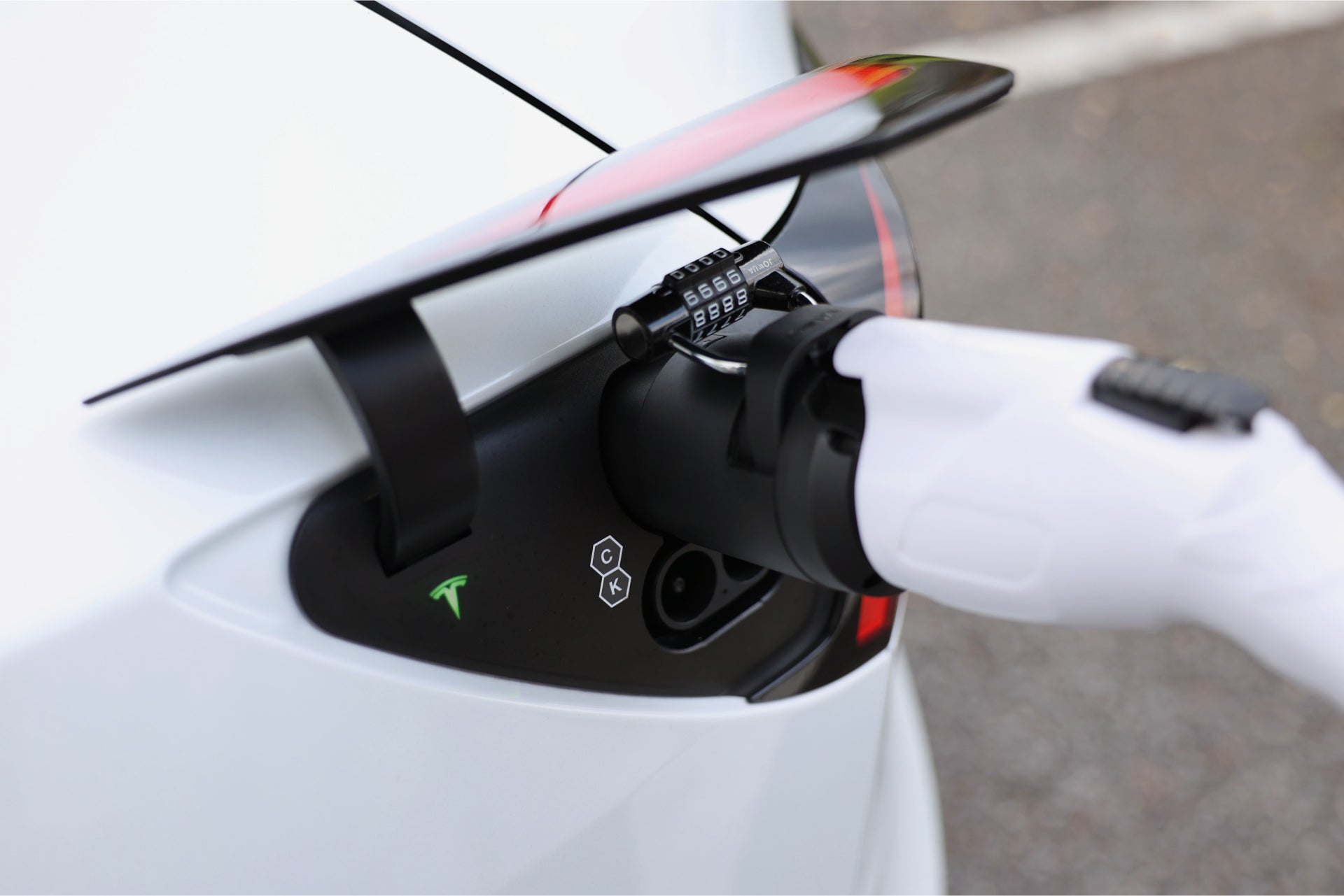使用 JOWUA Taiwan CCS2 快慢充萬用組(通用版)充電的白色電動車特寫。白色充電插頭以密碼鎖連接至連接埠,附近可見 Tesla 標誌。.