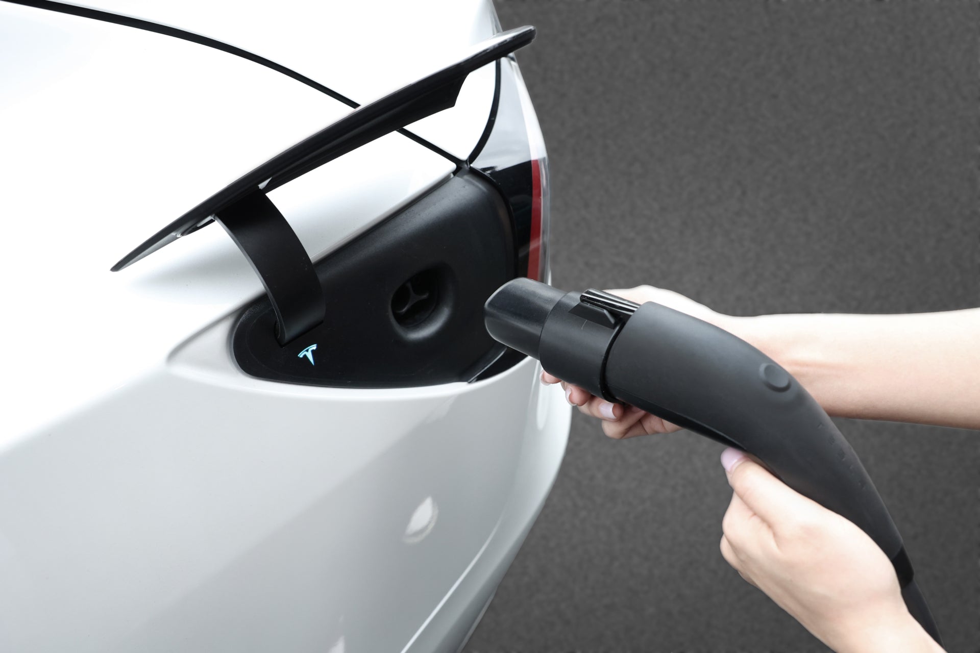 將 JOWUA 台灣 J1772 至 TPC(NACS) 轉接頭插入電動車。白色車輛的充電口位於後部,深色背景強調了 SAE J1772 充電過程。.