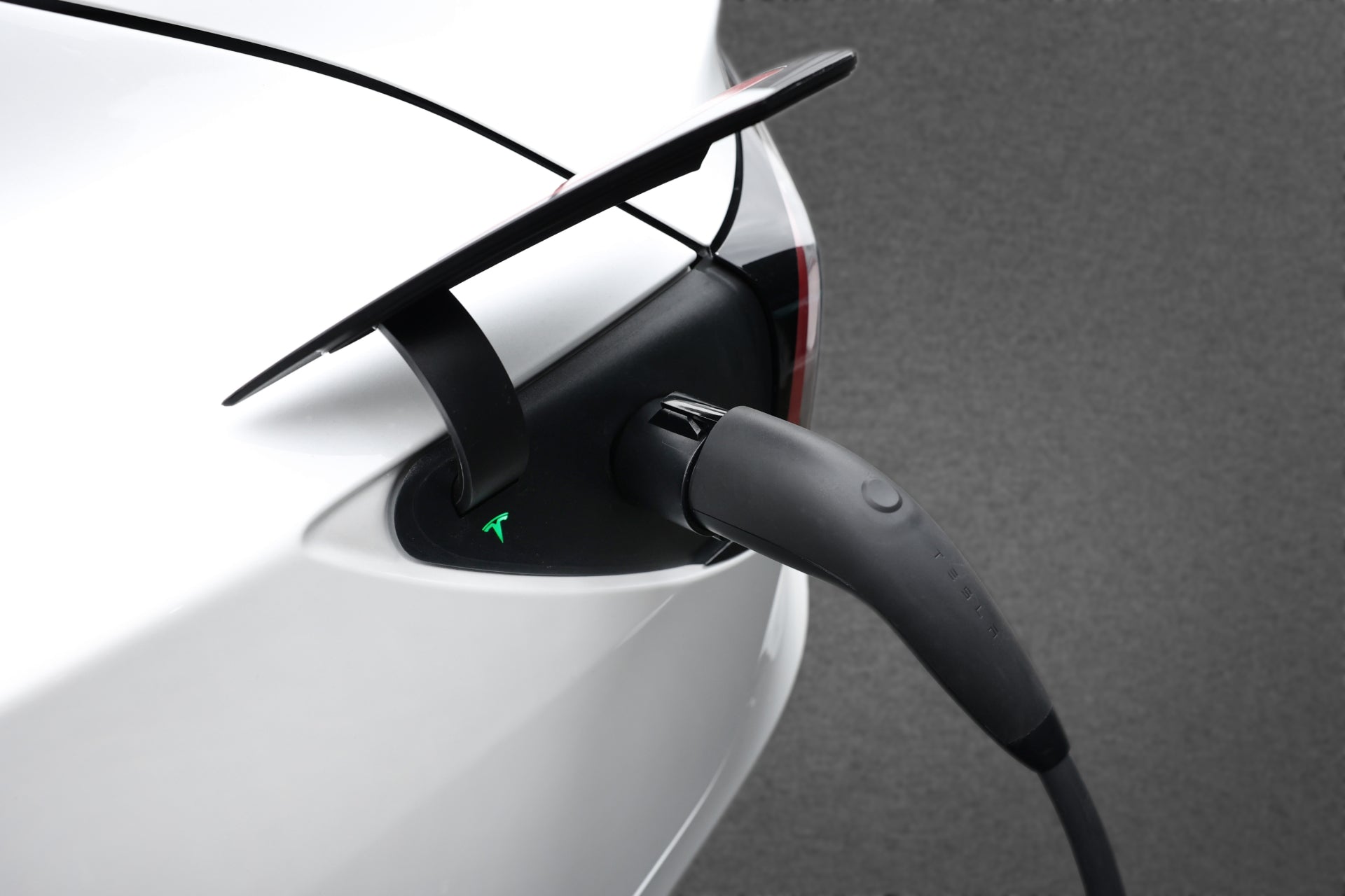 一輛白色電動車的開放式充電埠連接到JOWUA台灣J1772至TPC(NACS)轉接頭轉接器。插入了黑色電纜,與 1 型充電器相容,背景為純灰色。.
