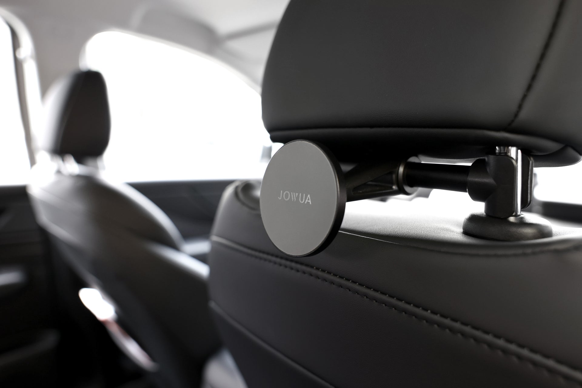 車內頭枕桿上展示JOWUA台灣通用型MagSafe磁吸掛鉤組。圓形黑色支架採用尼龍矽膠實現安全抓握,略微模糊的背景突出了時尚的設計。.