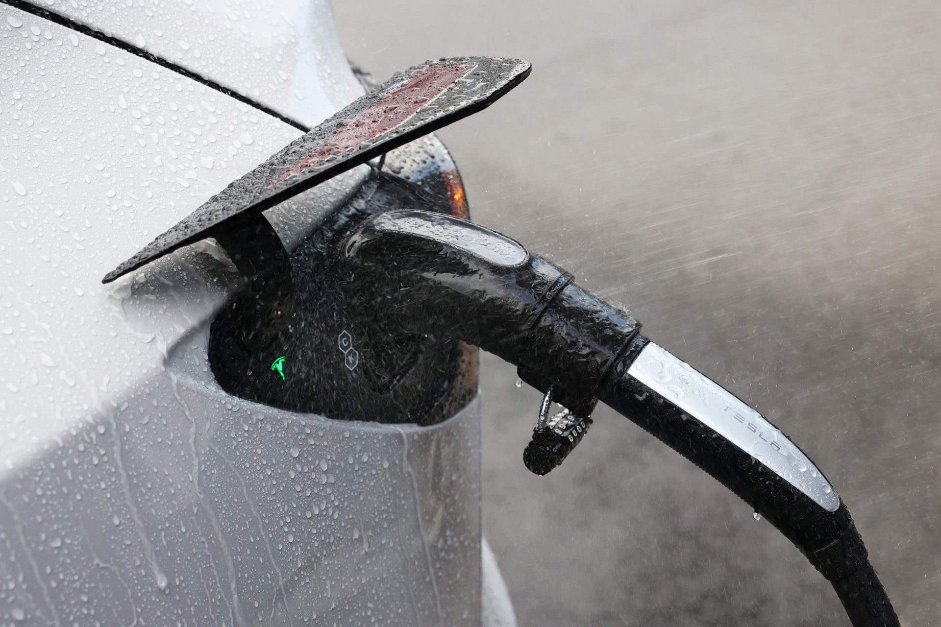 台灣 JOWUA CCS2 DC & AC 快慢充萬用組在雨中為電動車充電的特寫,車輛和電線上的水滴清晰可見,充電口附近有綠色指示燈。.