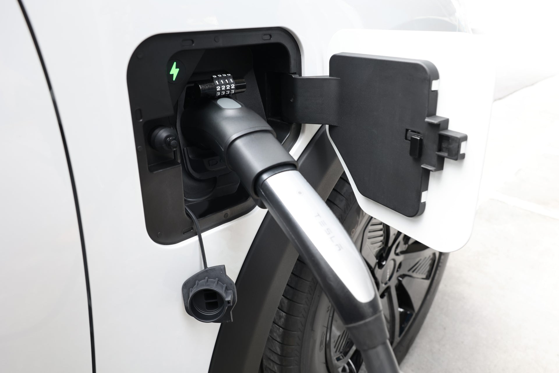 台灣 JOWUA 的 CCS1 快慢充萬用組插頭連接到電動車充電埠的特寫。白色車輛支援第三方網路相容性,可實現多功能充電。端口下方懸掛著一個黑色的蓋子,可以看到車輪。.