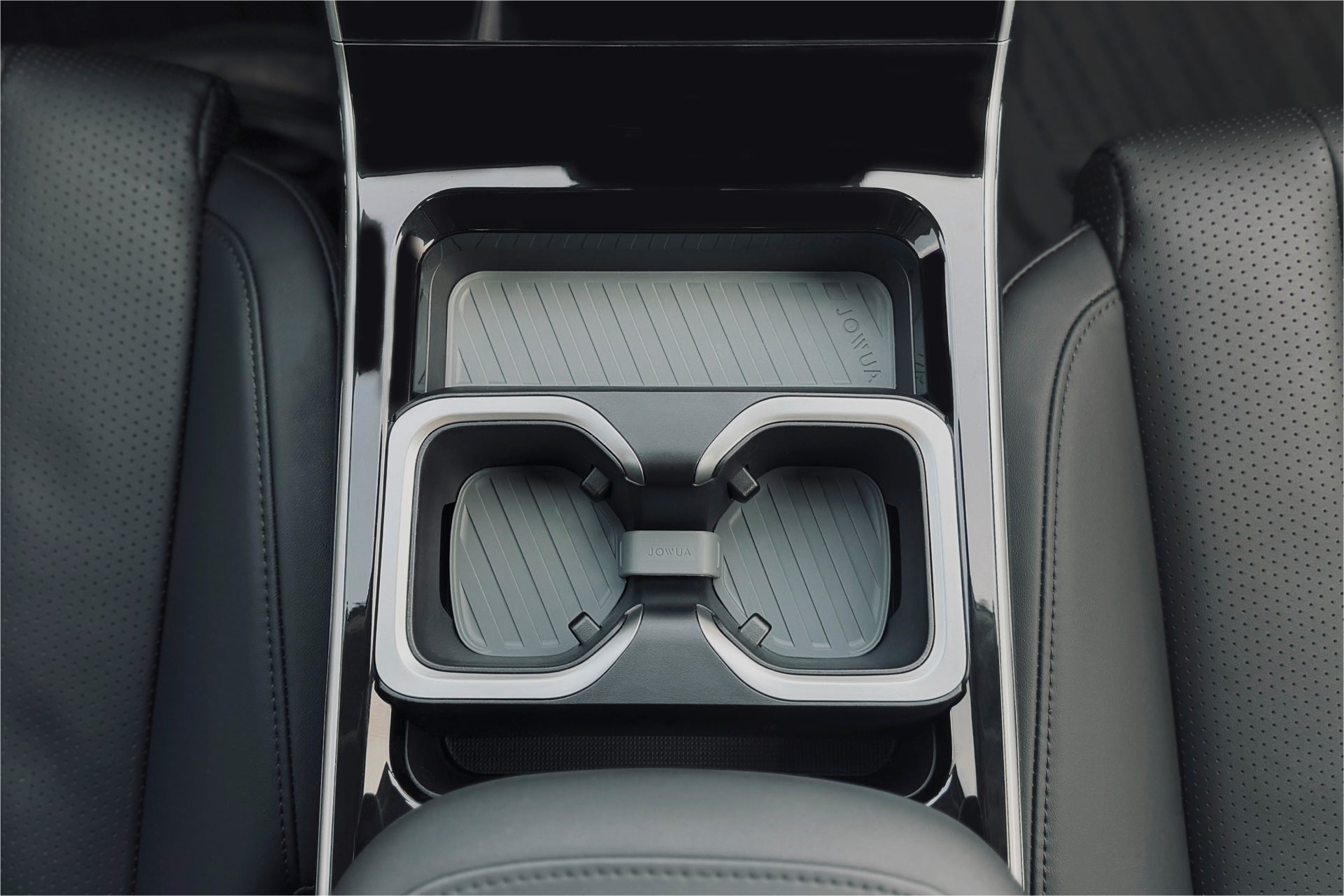 Luxgen n⁷ 汽車中控台的俯視圖,配有兩個帶有紋理嵌件的 JOWUA 台灣杯架組。光滑的黑色表面與附近的深色穿孔皮革座椅相得益彰,凸顯了精緻的汽車配件。.