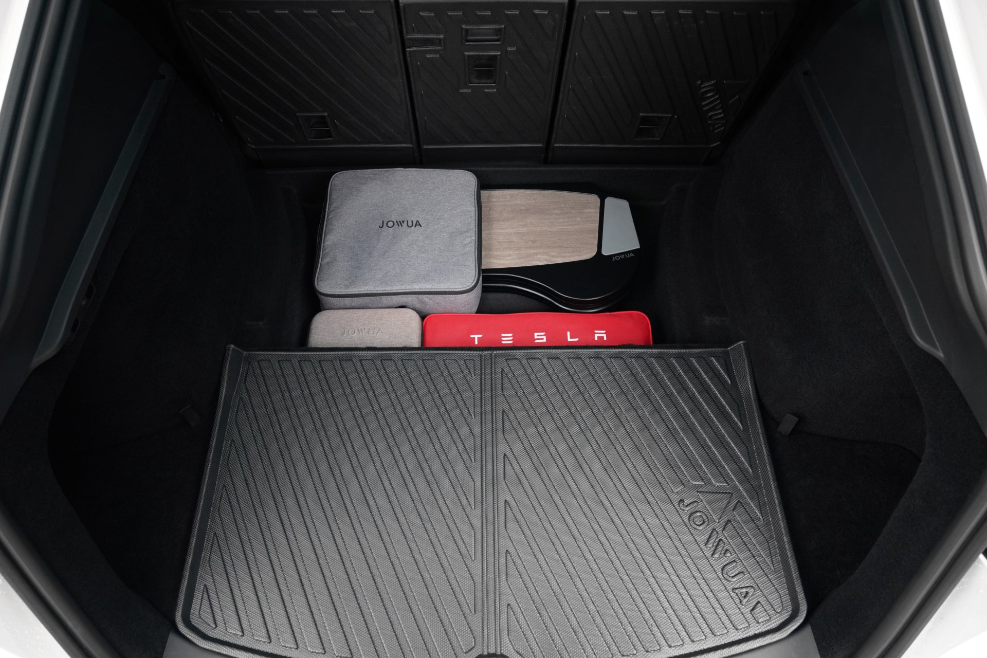 黑色 JOWUA Taiwan 行李廂全套組合 (Model Y 煥新版 2025+/2021-2024) 的汽車行李廂內,整齊堆放著 Tesla 配件、灰色、黑色和紅色防水行李廂收納盒,以及一塊木質面板。.