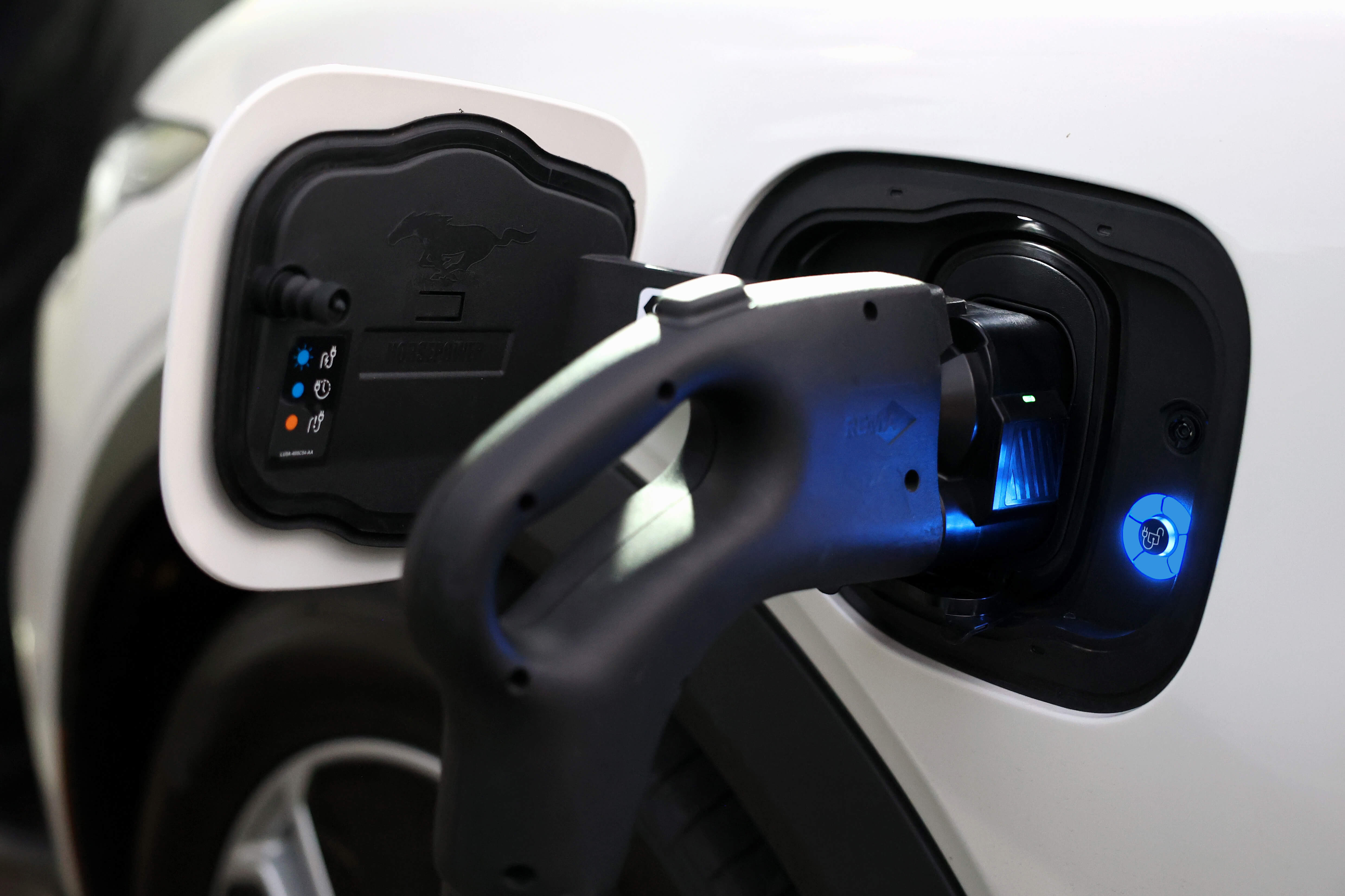 Mustang 充電埠特寫,JOWUA 台灣 CCS2 快慢充萬用組(通用版)已插入。插上後,指示燈亮起,開啟的蓋子上可見 Mustang 標誌。.