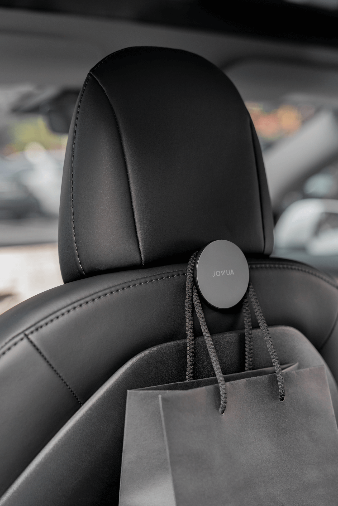 時尚現代的黑色汽車座椅頭枕配有 JOWUA 台灣掛鉤組 (Model Y),非常適合放置灰色購物袋。時尚的皮革內裝與椅背掛鉤的功能完美融合。.
