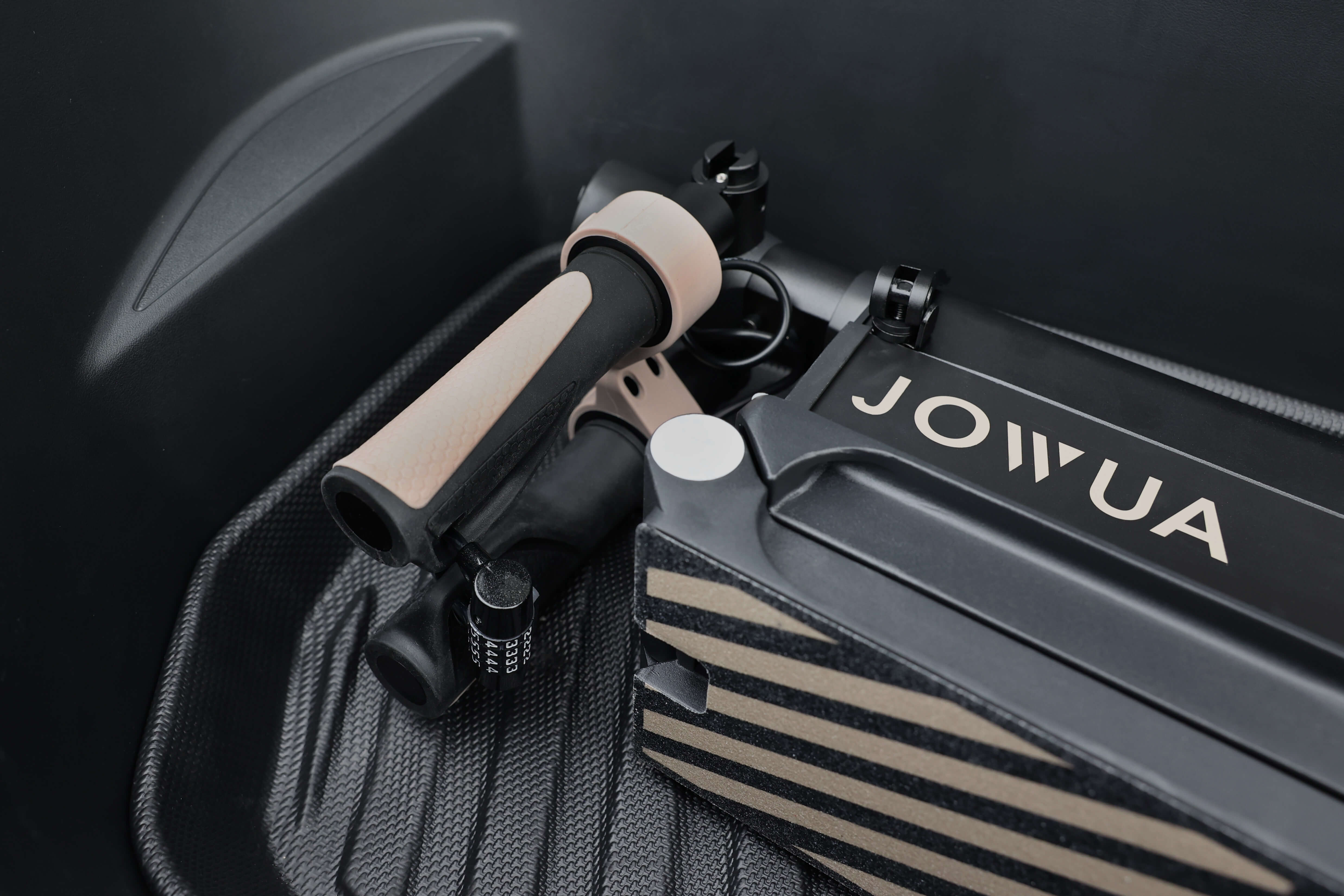 JOWUA Taiwan 折疊電動滑板車|LRR 車把上的防盜手把特寫,與黑色「JOWUA」盒子一起展示,兩者都放置在黑色紋理表面上。.