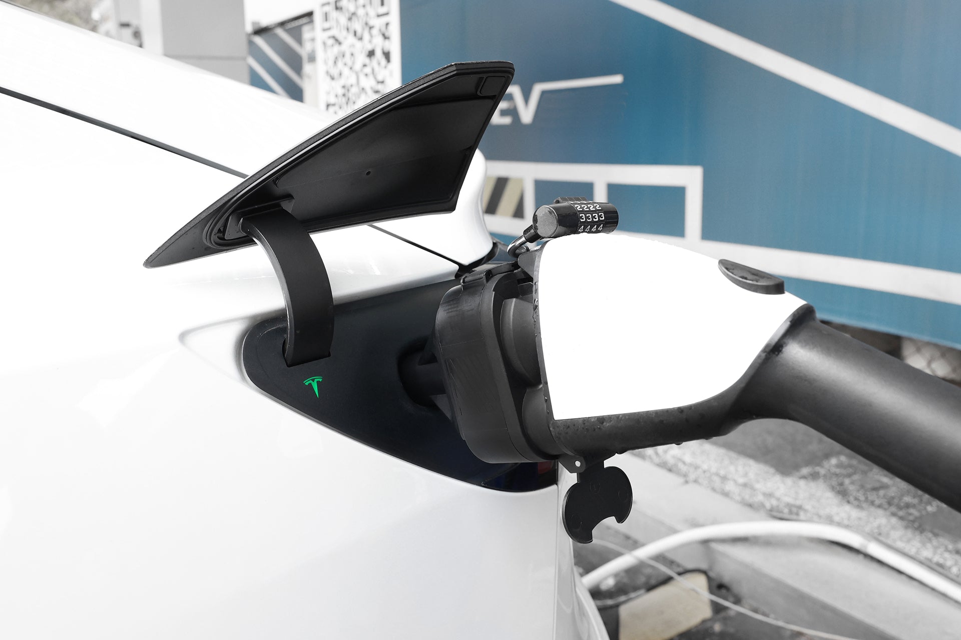 特寫顯示一輛白色電動車使用 JOWUA Taiwan CCS1 to NACS (TPC) DC & AC 快慢充轉接頭,充電蓋板打開,後方是藍色的 EV 充電站,突顯特斯拉充電的相容性。.