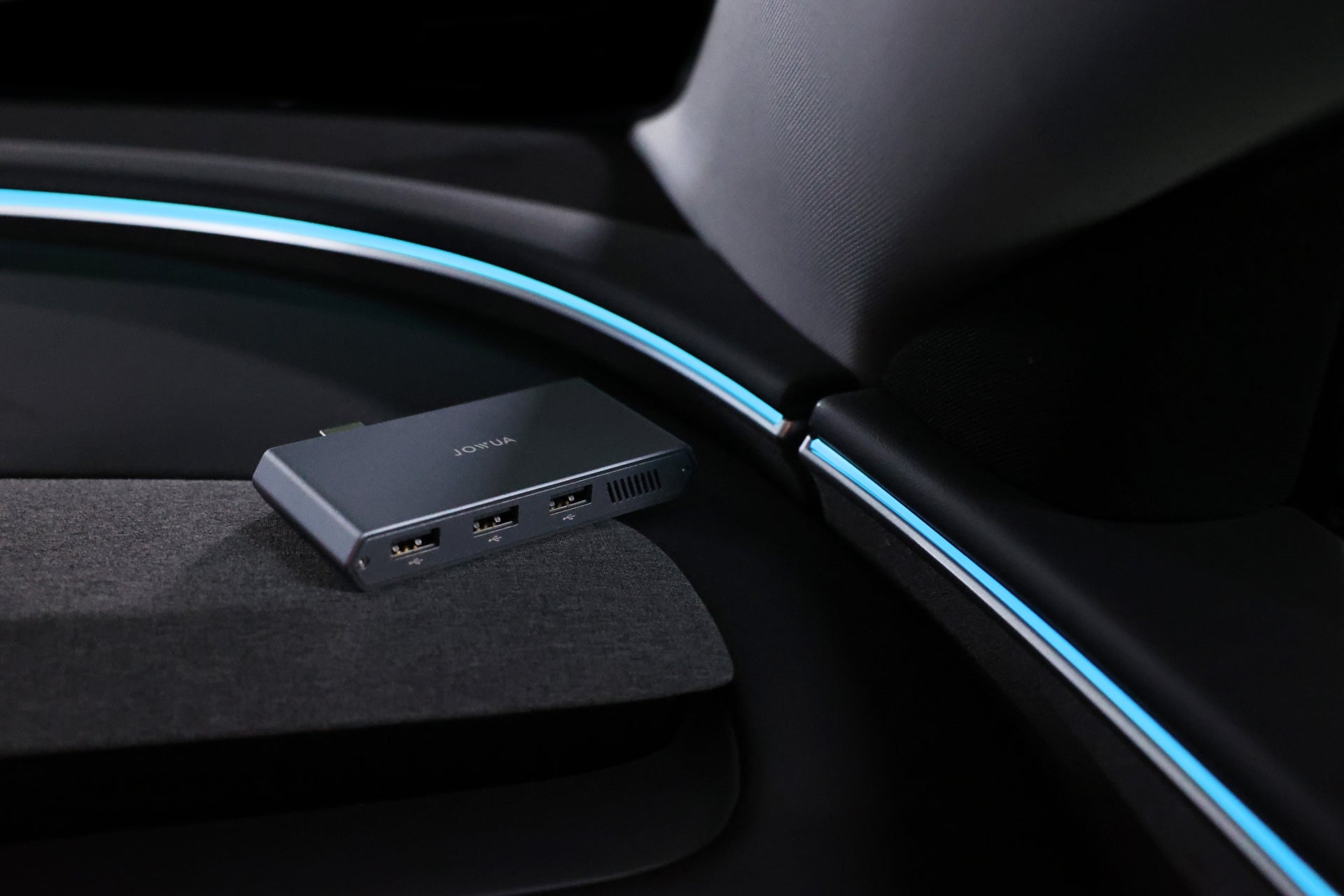時尚的 JOWUA 台灣 Tesla 專用 1TB SSD+3 連接埠 HUB 放置在現代 Tesla 內部的黑色表面上,周圍裝飾著藍色 LED 照明,透過這款多功能集線器增強連接性,營造出未來主義氛圍。.