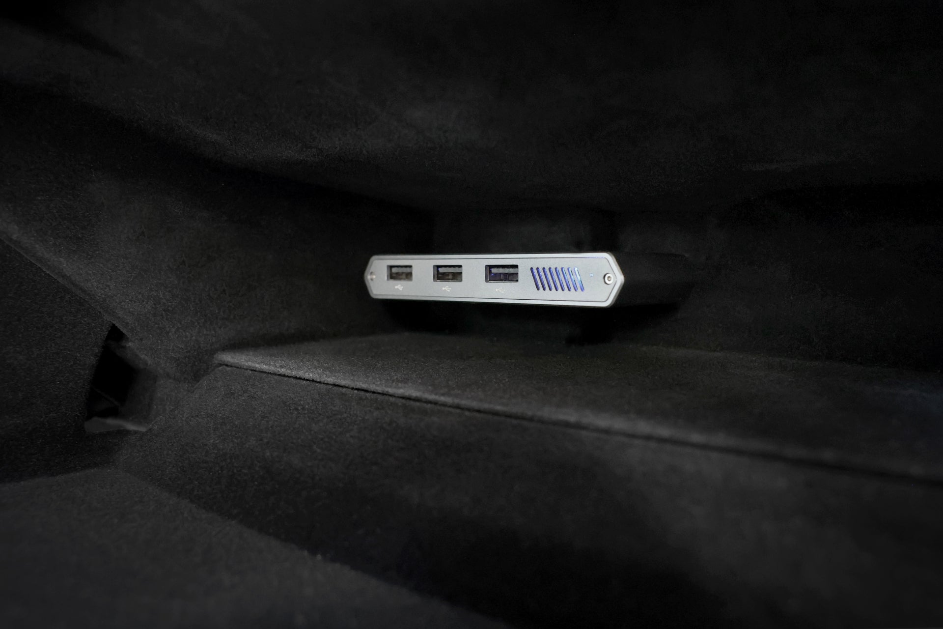 特斯拉車主手套箱特寫,展示了JOWUA台灣特斯拉專用1TB SSD+3端口HUB,具有三個可見端口和藍色條紋設計,與深色內飾形成鮮明對比。.