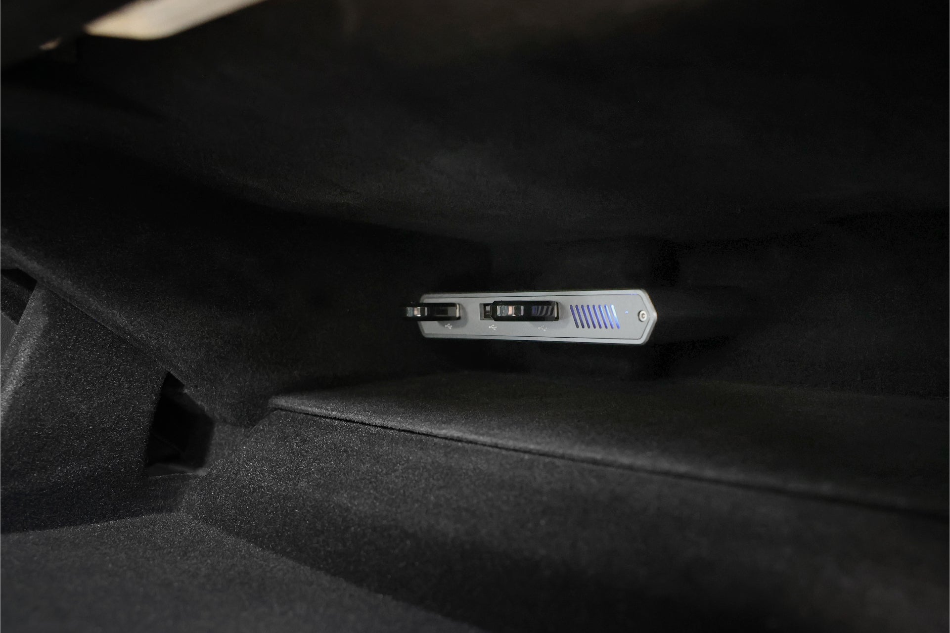 黑色車內裝特寫,展示的是JOWUA台灣特斯拉專用1TB SSD+3口HUB(Model S/X/Model 3煥新版2024+/Cybertruck),儀錶板下方配備NVMe驅動介面。它擁有時尚的金屬設計和藍色強調燈,非常適合挑剔的特斯拉車主。.