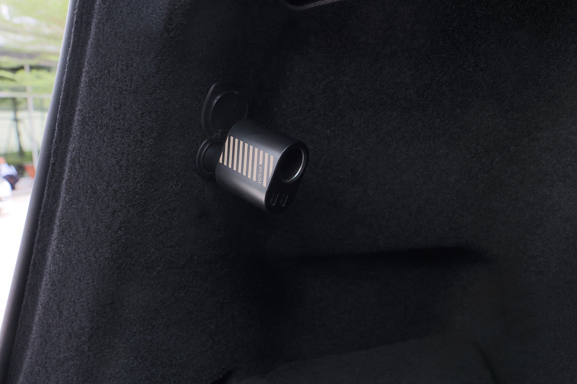 精巧的黑色儀表盤攝影機,搭配條紋設計,安裝在深色布料裝潢的車內。採用 JOWUA Taiwan 三合一 Type-C 擴充點菸器車充,完美滿足車用電力擴充需求。.