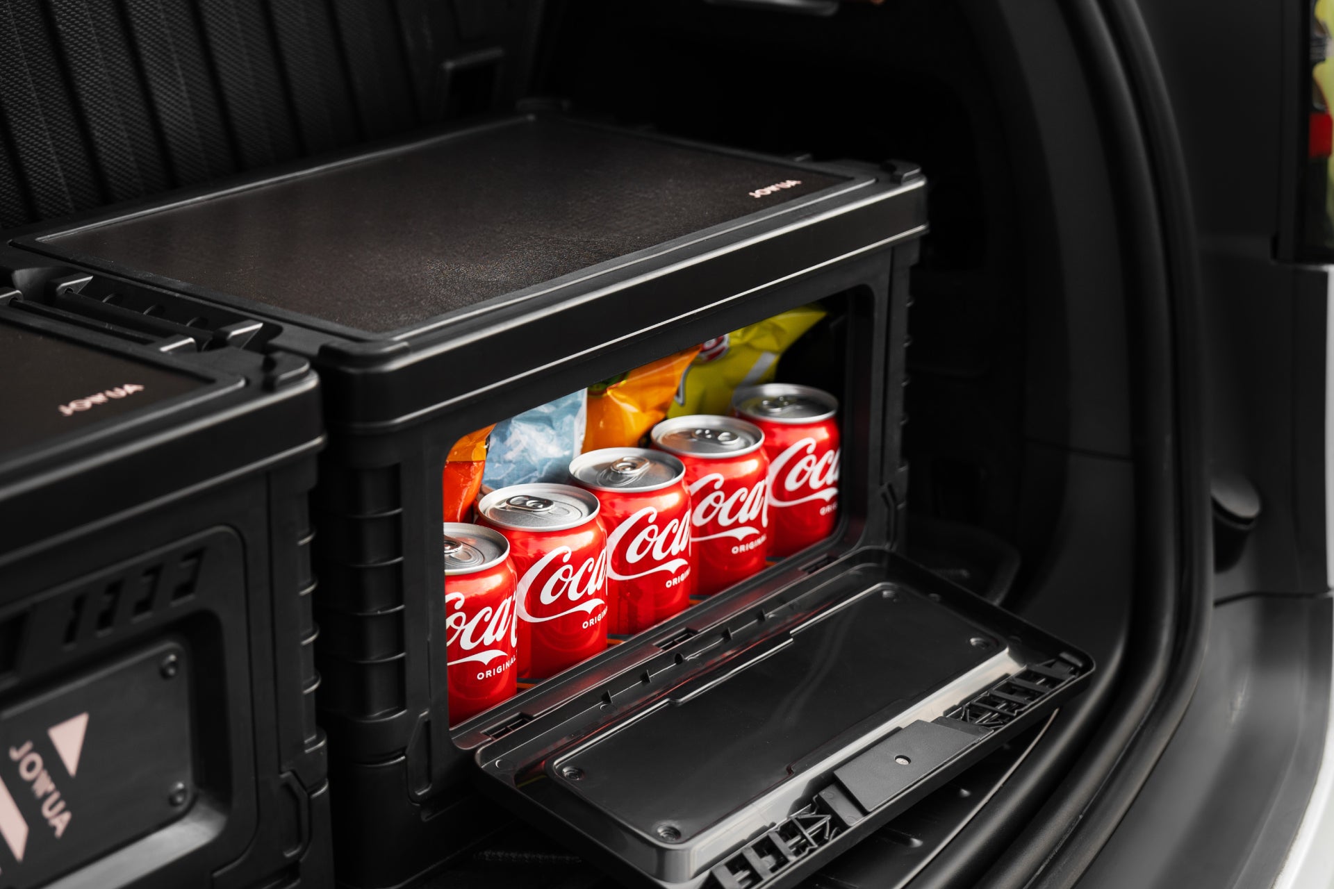 打開 Model X 的後行李箱,可以看到一個 JOWUA 台灣 30L 收納箱,裡面裝滿了可口可樂罐和零食袋,位置方便且視野清晰。內裝時尚、井然有序,並配有車用折疊桌板。.