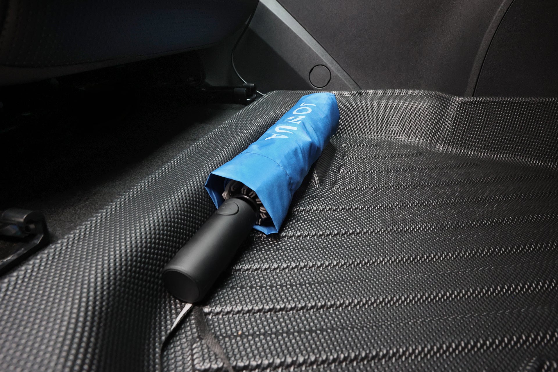 一把閉合的藍色傘子搭配黑色手柄,放置在以專利止擋收納設計為特色的 JOWUA Taiwan 立體防水腳踏墊 (Foxtron Bria) 車後座上。.