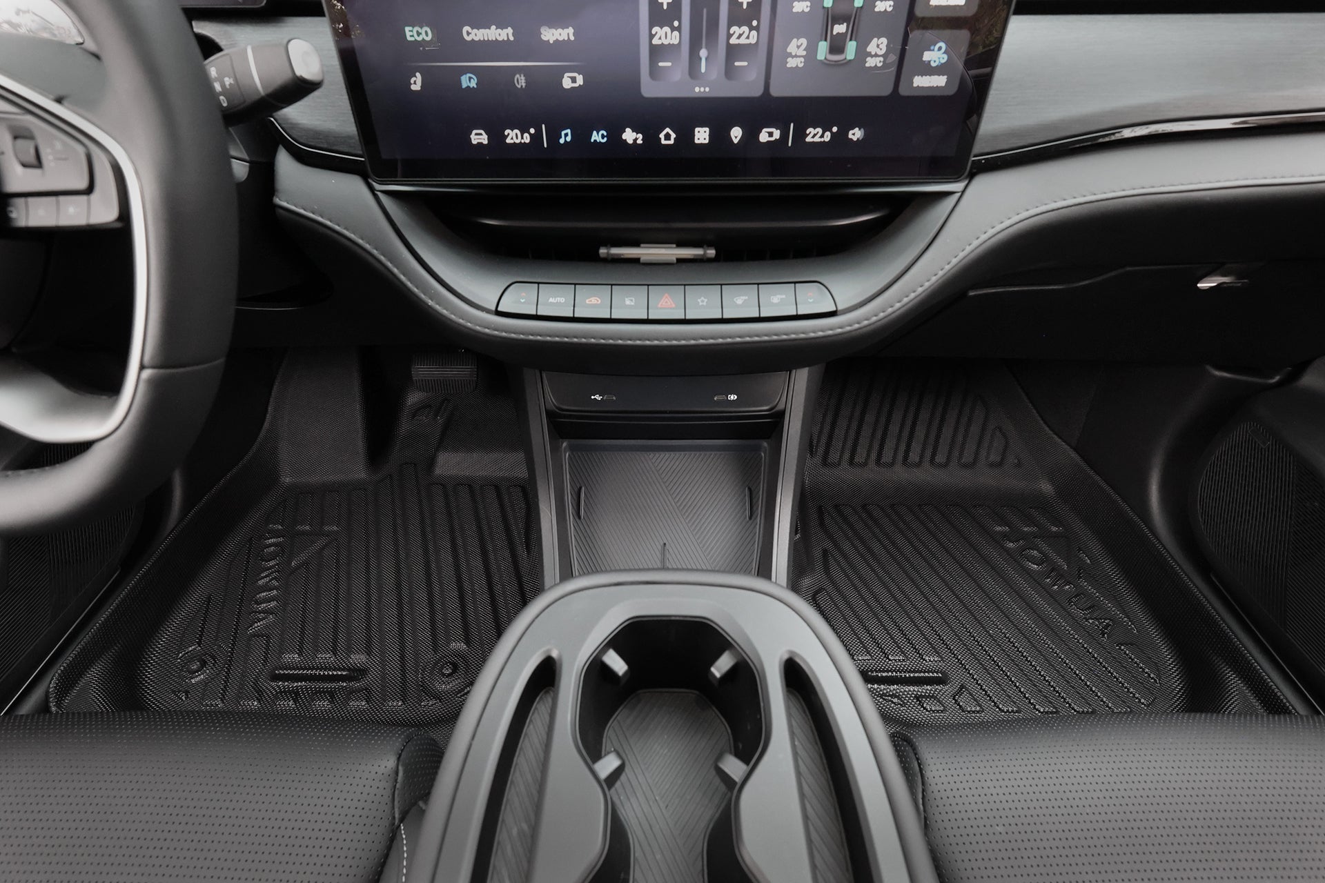 汽車中控台特寫,設有杯架、觸控螢幕和專利止擋收納設計的 JOWUA Taiwan 立體防水腳踏墊 (Foxtron Bria)。排檔桿與溫度控制按鈕也清晰可見。.