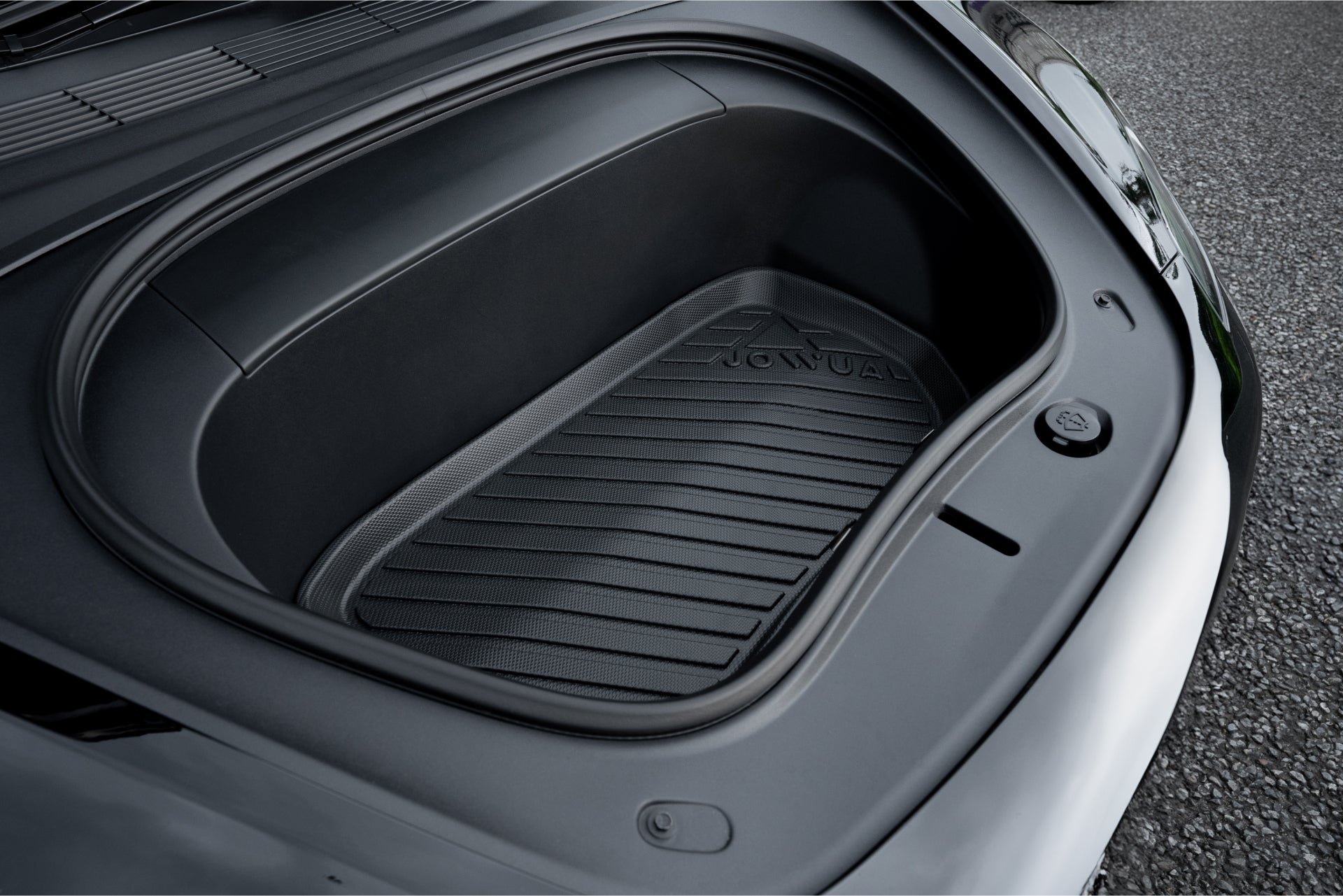 時尚的黑色特斯拉 Model 3 的開放式前行李箱露出由 JOWUA 台灣製造的紋理立體防水行李廂墊,是全天候保護的理想選擇。其光滑的外觀與碎石路面形成鮮明對比,為煥然一新的 Model 3 2024+ 設計增添了精緻感。.