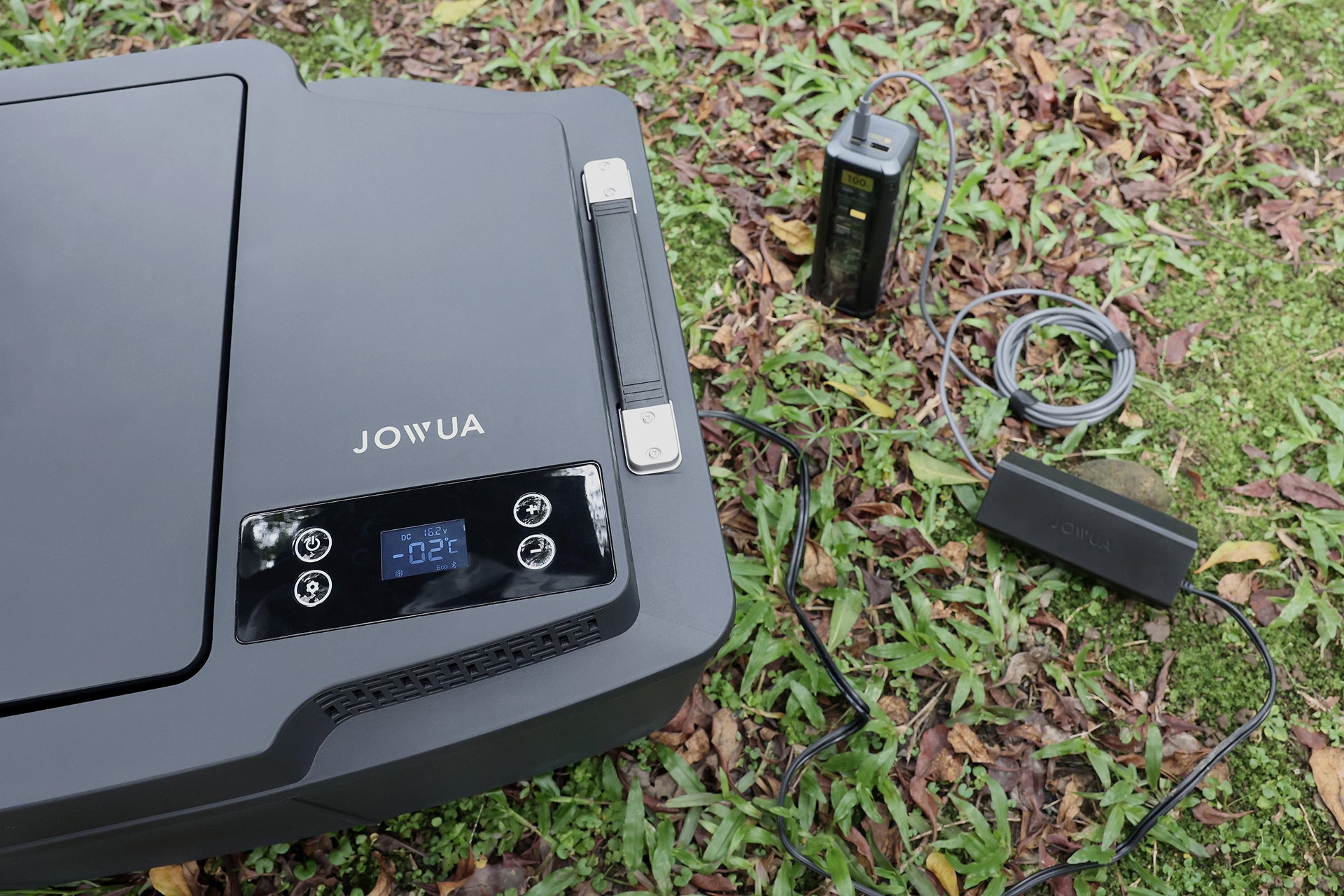 台灣 JOWUA Type-C 車用行動冰箱 (Model 3 全車系) 配備數位顯示器和 20L 容量,放置在草地上,可透過 Type-C 充電的電源供應器在戶外方便地供電。.