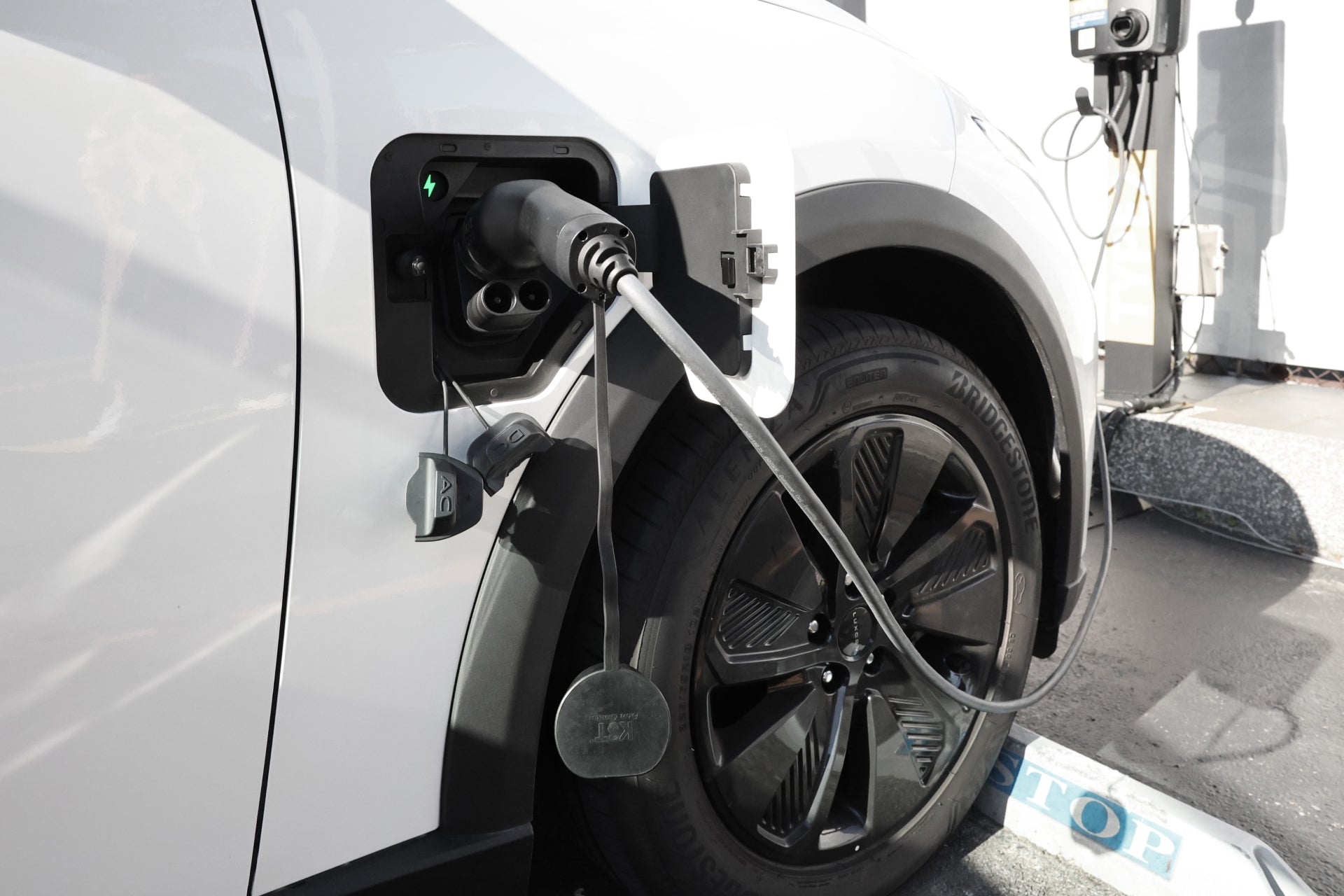 車站使用 JOWUA 台灣 CCS2 轉 CCS1 DC & AC 快慢充轉接頭的電動車特寫。充電器連接到引人注目的白色車輛的前端口,背景中可以看到充電站的溫度監控防護。.