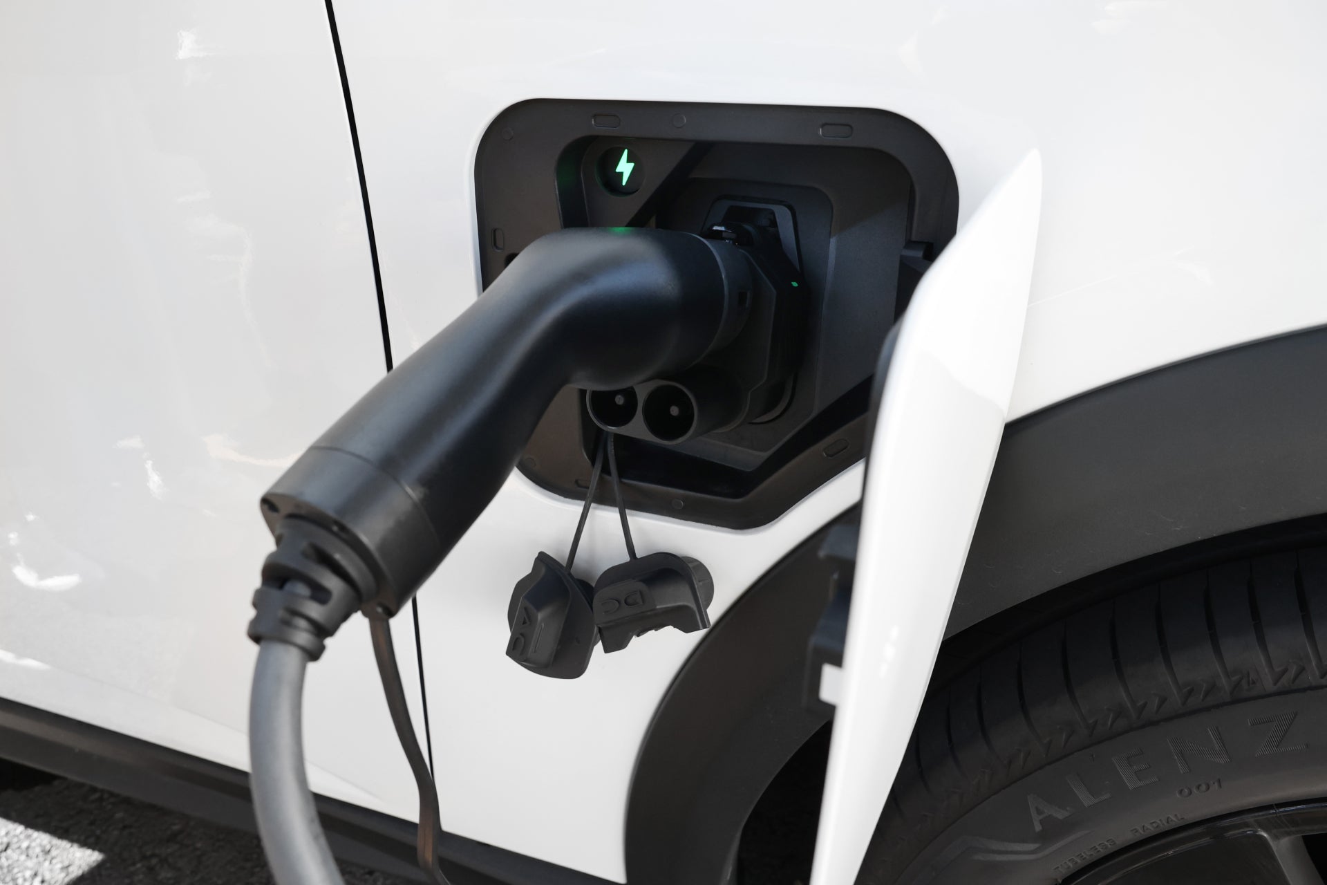 使用 JOWUA 台灣 CCS2 轉 CCS1 DC & AC 快慢充轉接頭的電動車特寫,顯示連接埠中的插頭帶有閃電符號。白色車身和輪胎清晰可見,快充慢充樁和溫度監控防護確保能量高效安全流動。.