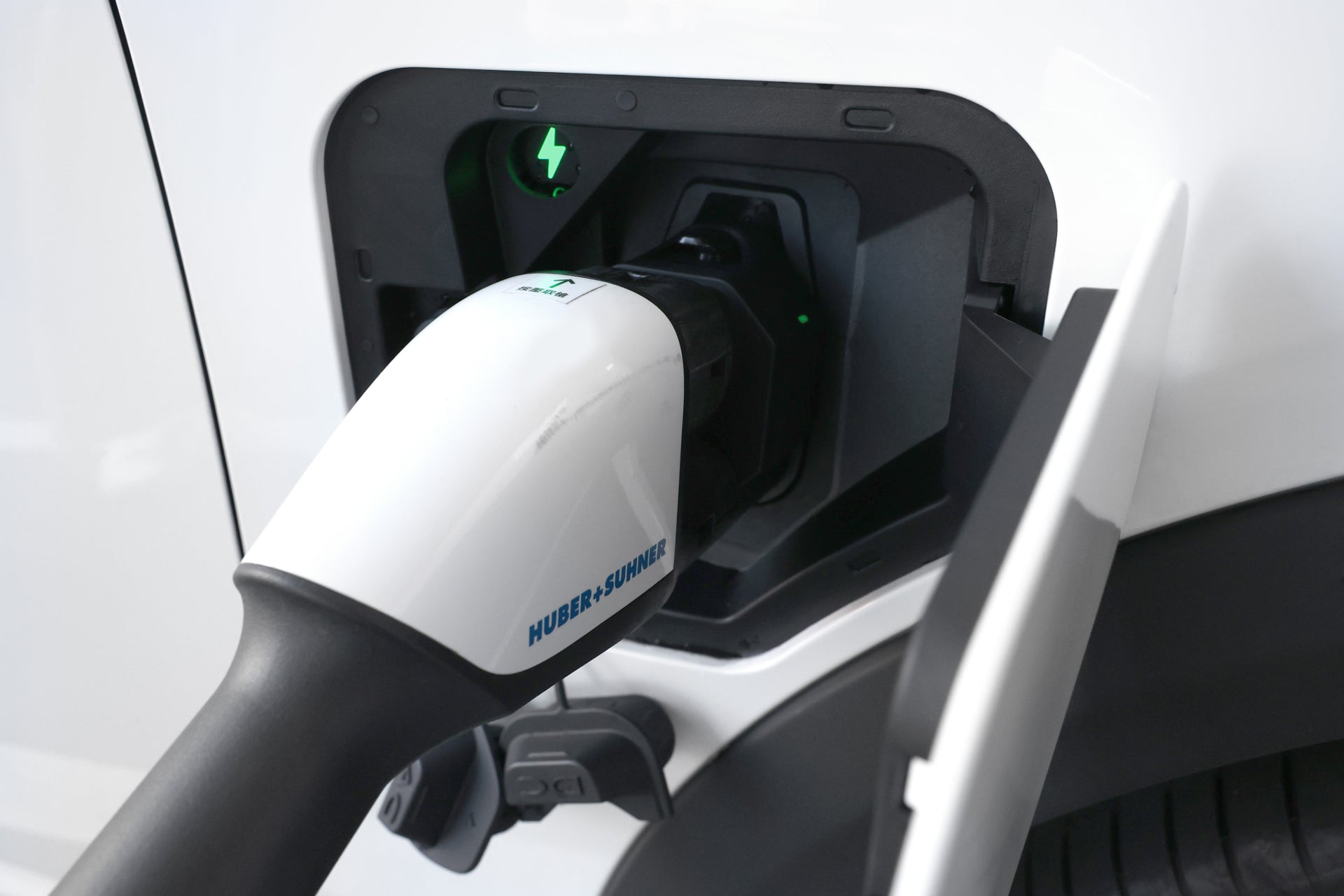 帶有白色電纜的電動車充電埠特寫,採用台灣 JOWUA CCS2 轉 CCS1 DC & AC 快慢充轉接頭,無縫相容。綠燈亮起表示正在積極充電,並採用先進的溫度監控防護措施,優化快充慢充充電樁的能源。.