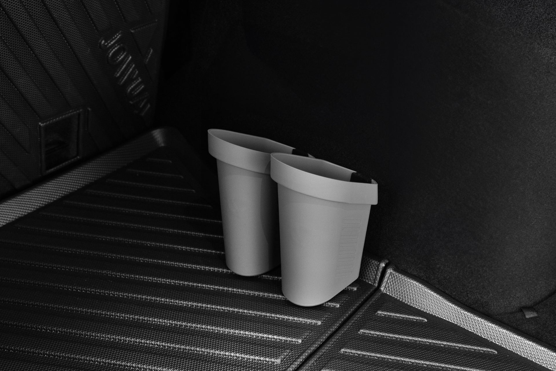 兩個杯架安裝在汽車內部帶有肋狀細節的黑色紋理表面上。昏暗的燈光凸顯了其時尚的設計,增強了車輛配件(如 JOWUA Taiwan 的車內萬用收藏桶(兩入一組))。.