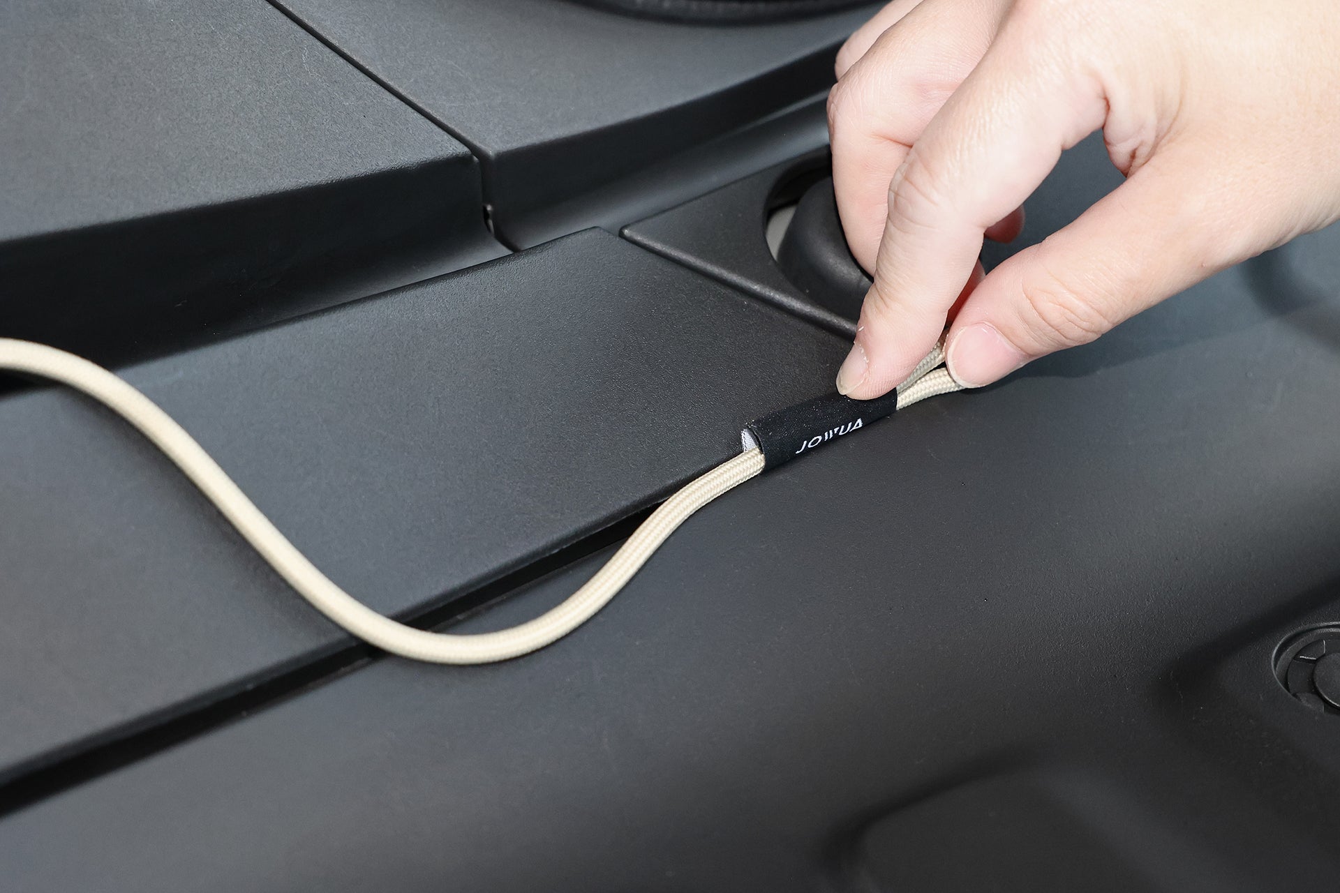 一手精確地將電纜插入JoltHub,呼應台灣JOWUA充電槍緊急釋放延長拉繩(LUXGEN n⁷)的設計精度。在柔和的燈光下,帶有黑色連接器的米色電纜在霧面表面上顯得格外突出。.