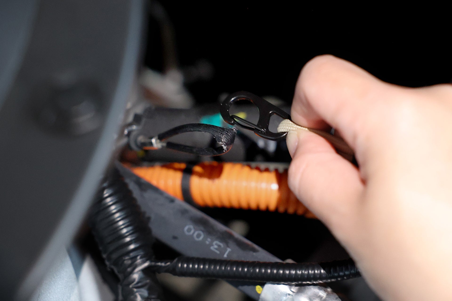 特寫鏡頭顯示一隻手使用 JOWUA 台灣充電槍緊急釋放延長拉繩將黑色紮帶連接在橙色和黑色電線上,可能是在納智捷LUXGEN n⁷這樣的汽車環境中。模糊的背景突出了手和電纜,確保所有元素保持清晰。.