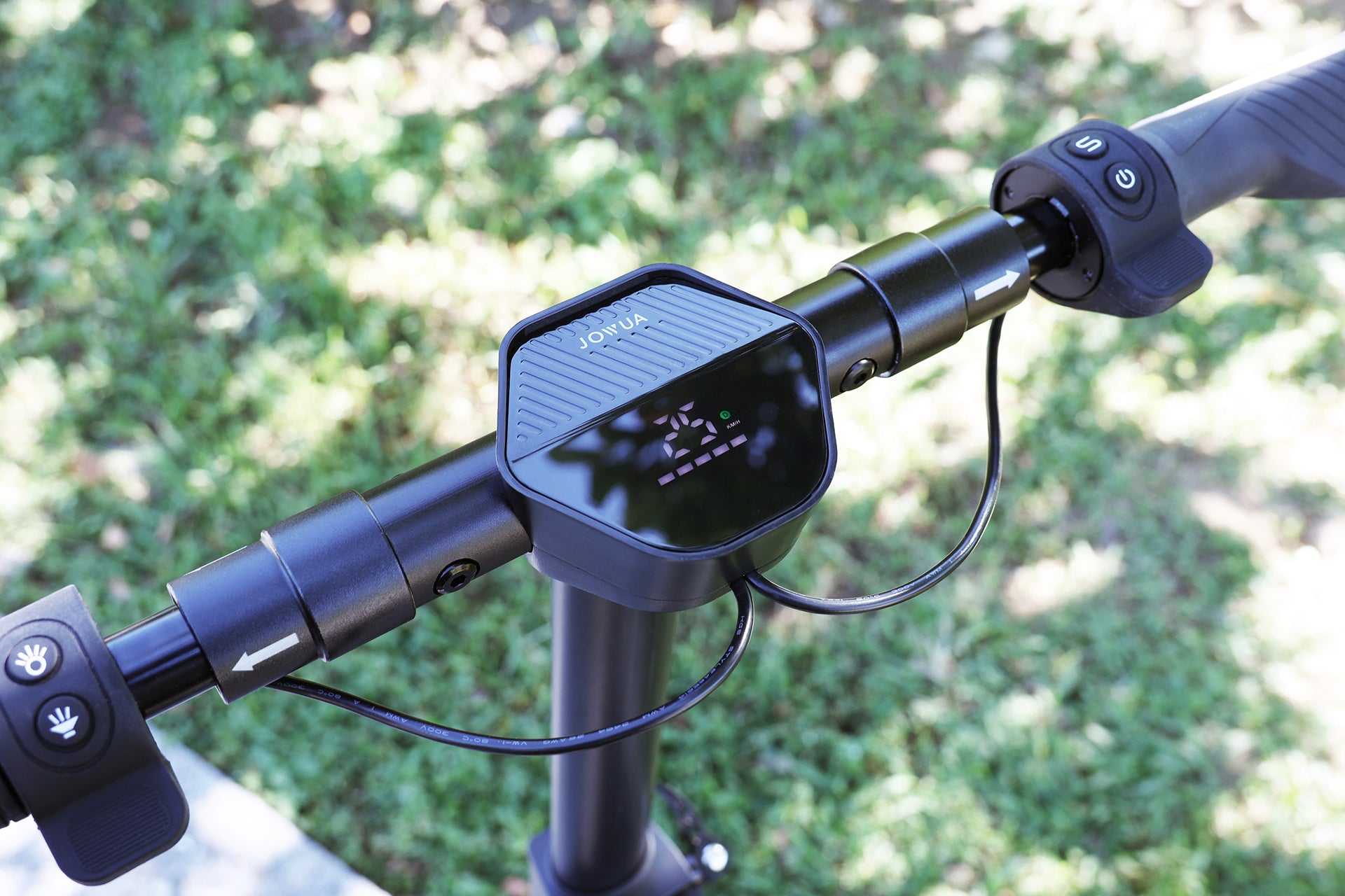 JOWUA Taiwan 折疊電動滑板車|高性能手把,配備數位顯示、電源按鈕和控制裝置。升級的電池容量升級,確保更長的騎乘時間,以模糊的草地背景展示,增加便利性。.