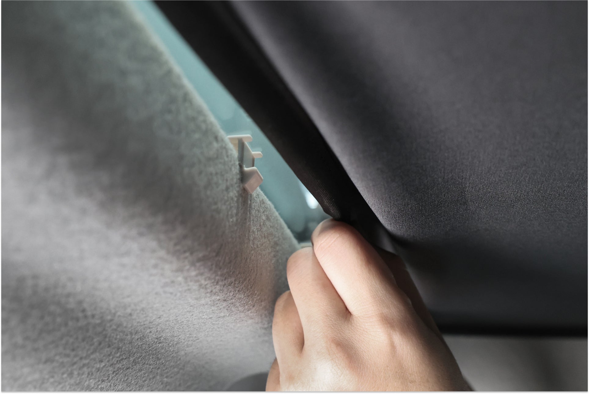 一手輕輕拉開 LUXGEN n⁷ 的玻璃車頂遮陽簾,露出了其車頂結構。這張圖像展示了一個紋理表面,並用 JOWUA 台灣黑武士夾子固定它,自然光柔和地照亮了場景。.