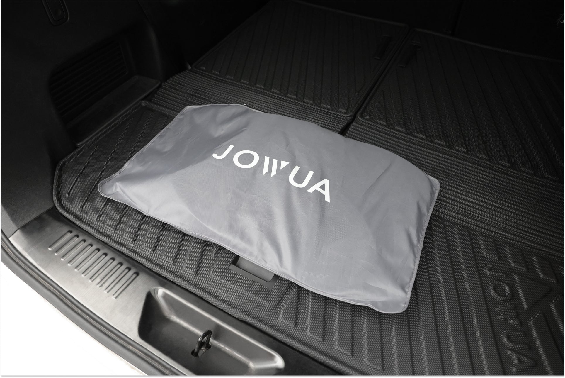 一個折疊的灰色袋子上印有“JOWUA Taiwan”字樣,放置在光滑的黑色橡膠汽車後備箱墊上,與 LUXGEN n⁷ 車輛的玻璃車頂遮陽簾的精緻風格相呼應。.